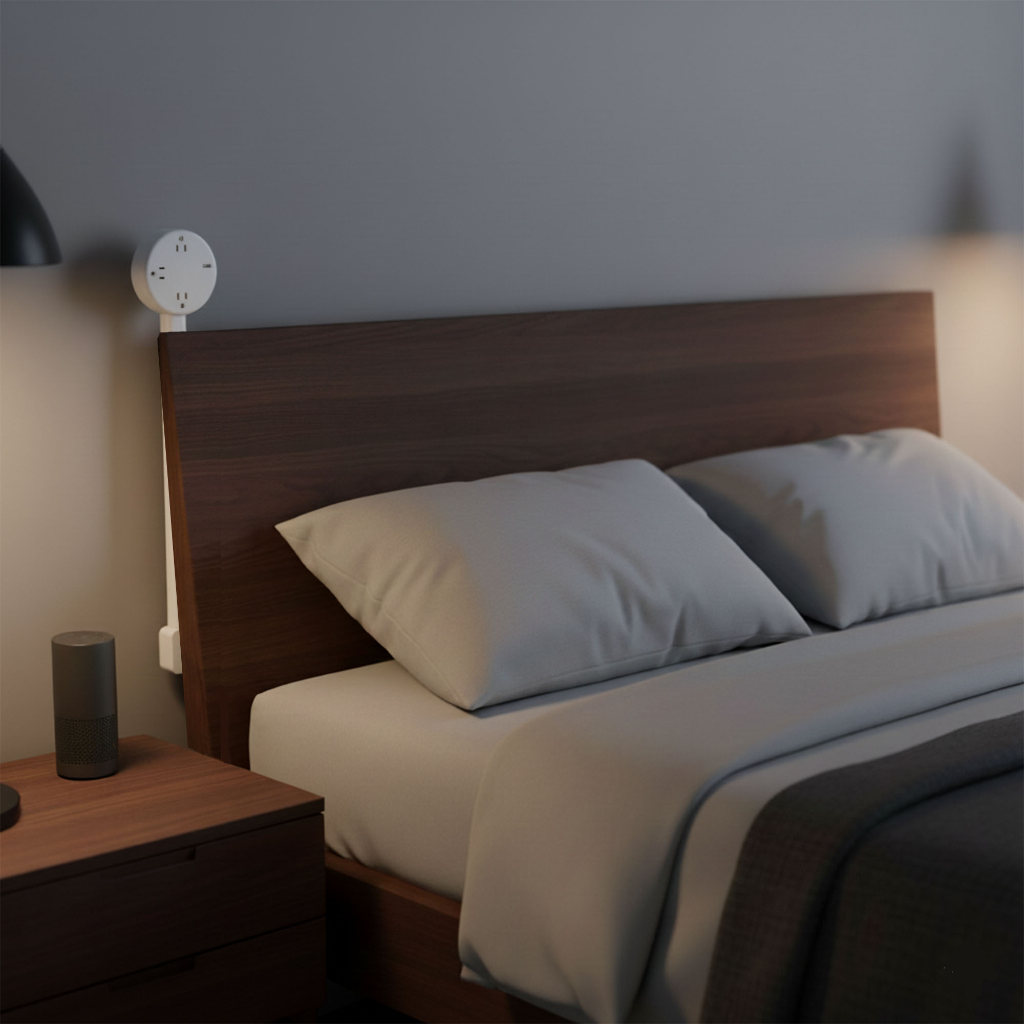 Schlafzimmer mit Bett, Nachttisch und Steckdose. Kissen und Decke auf dem Bett. Ein Lautsprecher steht auf dem Nachttisch.
