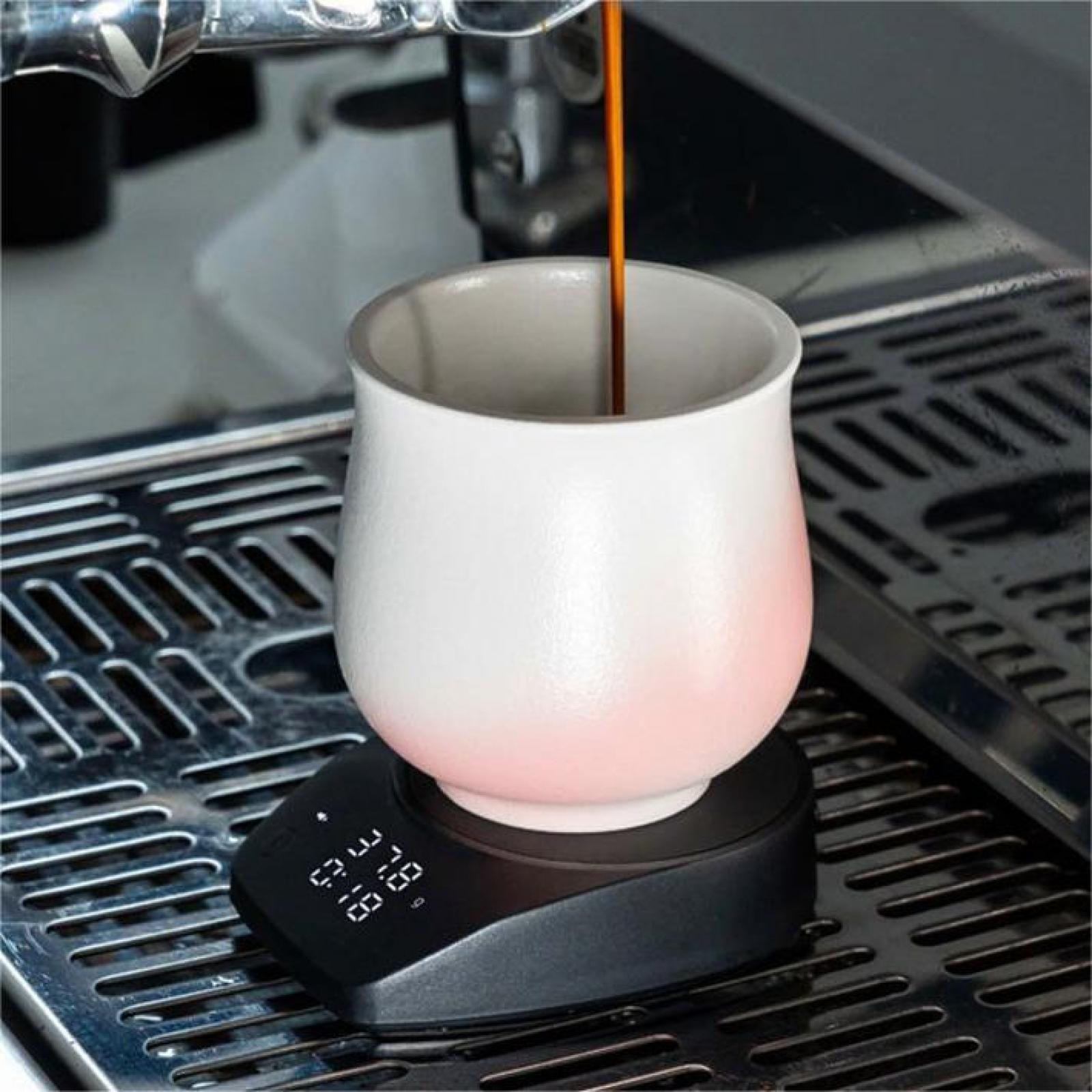 Espresso gießt in eine weiße Tasse auf einer Waage. Die Tasse hat einen rosa Farbverlauf. Die Umgebung ist eine Kaffeemaschine.