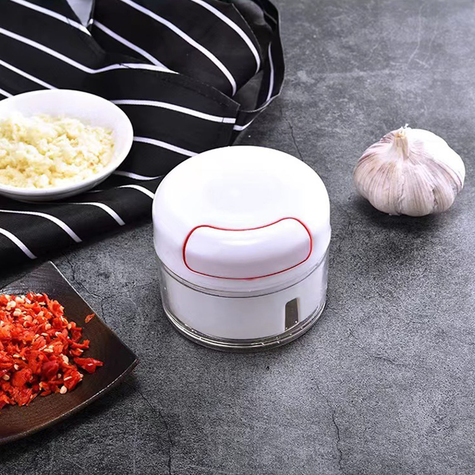 Ein weißer Knoblauchhacker, Knoblauch, gehackter Knoblauch in einer Schüssel und gehackte rote Paprika auf dunkler Oberfläche.