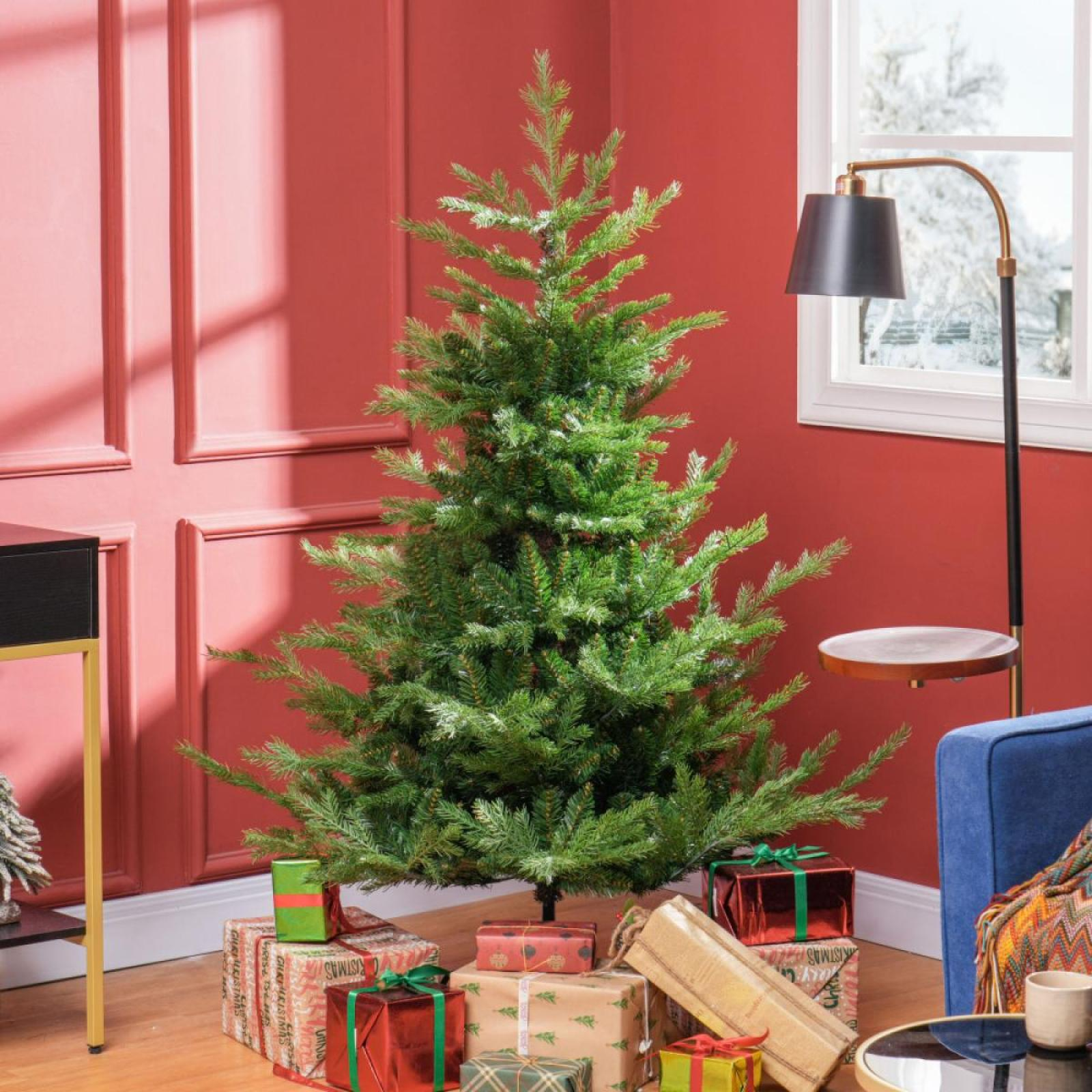 Ein grüner Weihnachtsbaum ist von verpackten Geschenken umgeben. Rote Wand, eine Lampe und ein Fenster mit verschneiter Aussicht sind im Hintergrund.