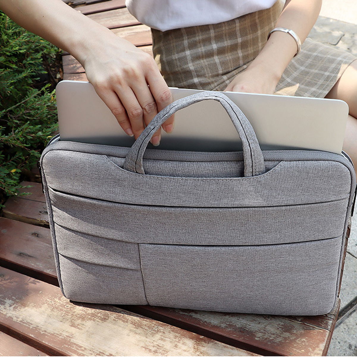 Eine Person hält eine graue Laptoptasche mit einem Laptop darin. Die Person sitzt auf einer Holzbank.