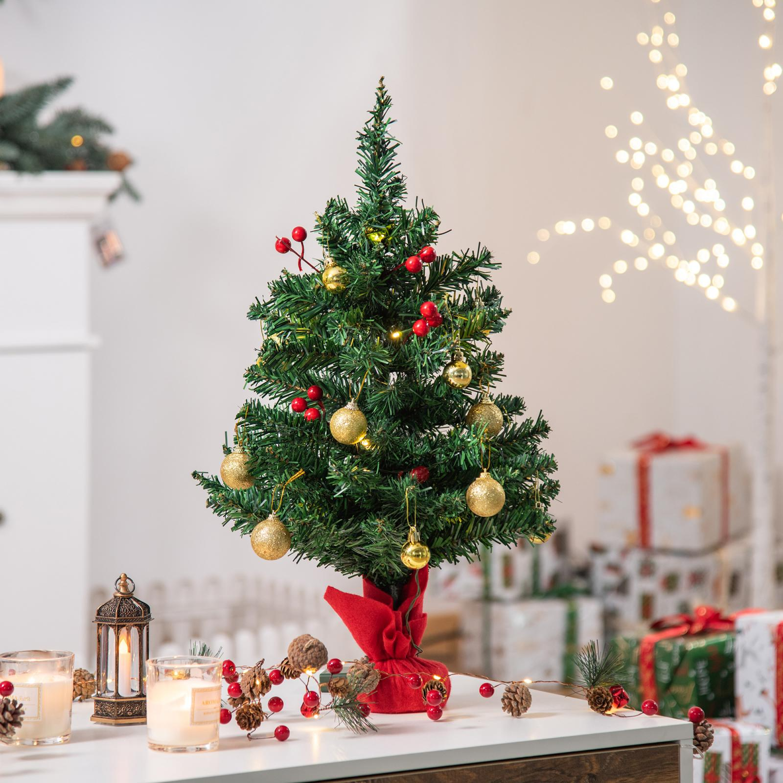 Ein geschmückter Weihnachtsbaum mit Ornamenten, Beeren und Lichtern auf einem weißen Tisch. Geschenke und Lichter im Hintergrund.