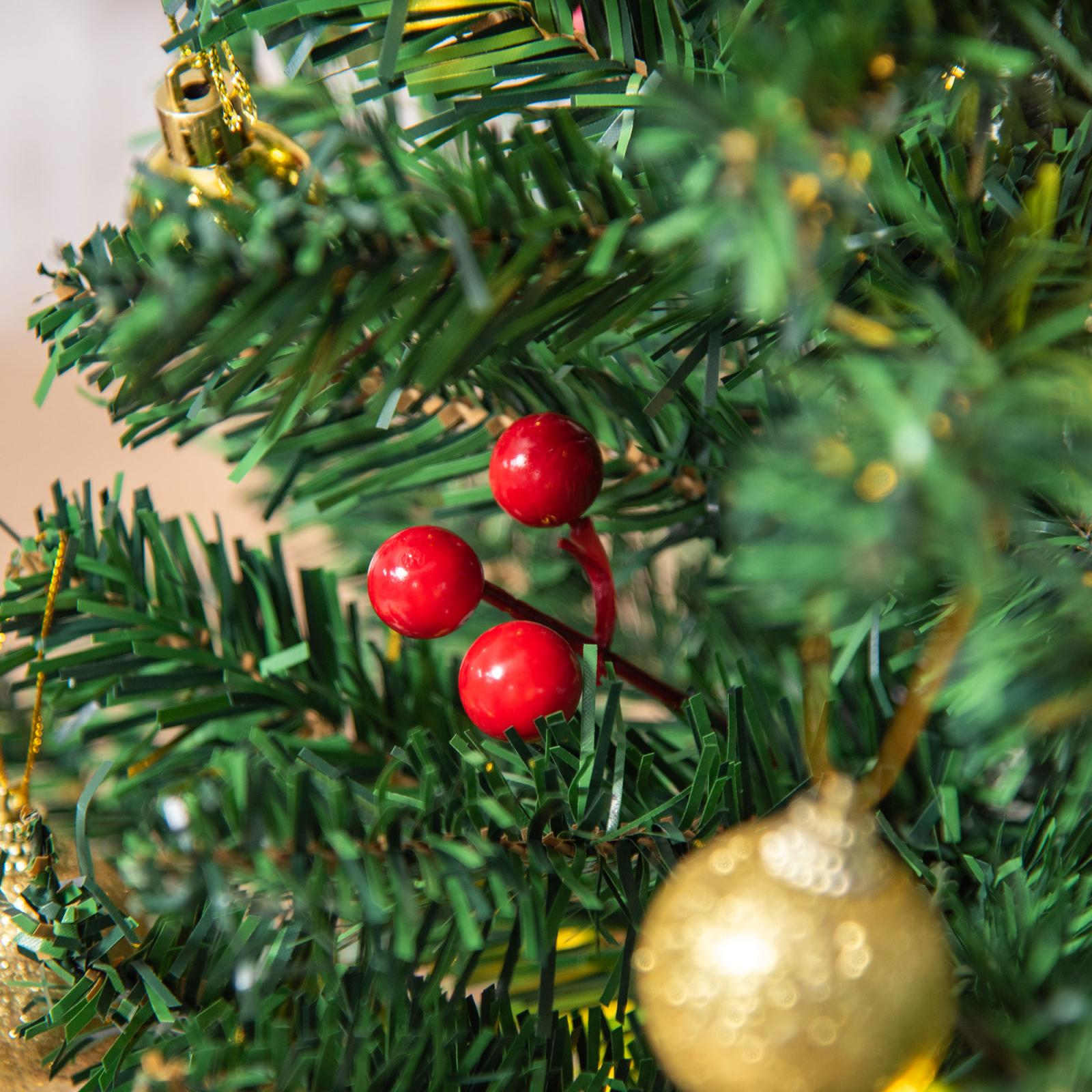Nahaufnahme eines Weihnachtsbaums mit roten Beeren und goldenen Ornamenten. Grüne Nadeln bilden den Hintergrund.