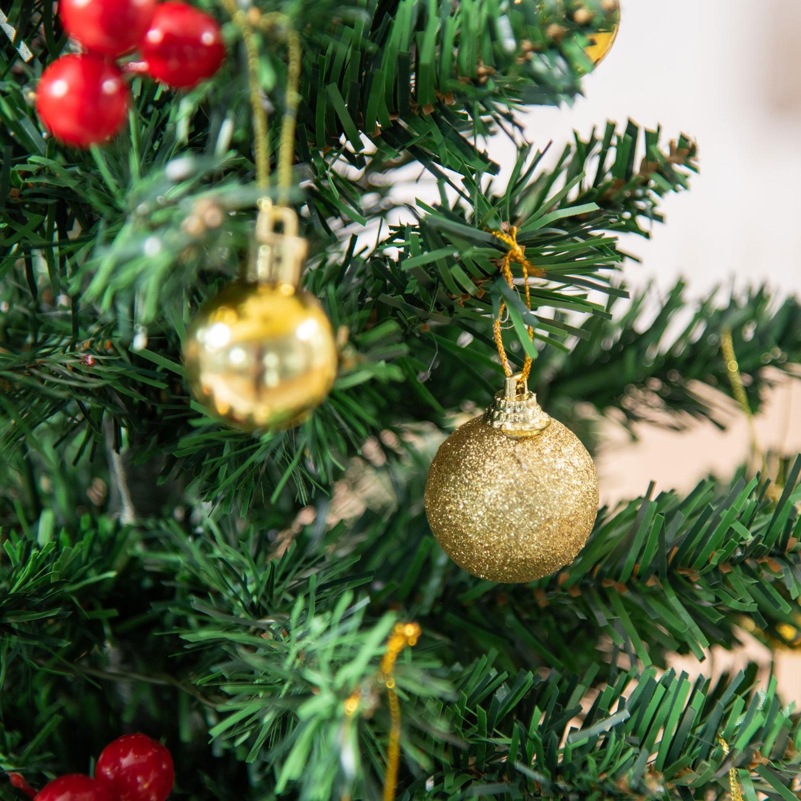 Nahaufnahme eines Weihnachtsbaums mit goldenen Ornamenten und roten Beeren. Grüne Nadeln füllen den Rahmen.