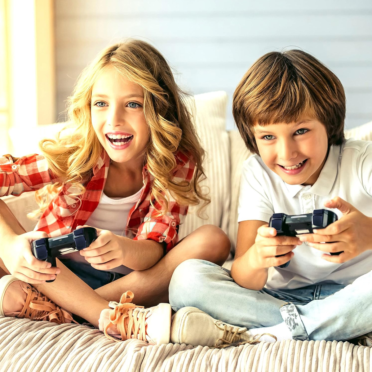 Zwei lächelnde Kinder spielen Videospiele und halten Controller. Ein Mädchen trägt ein rot kariertes Hemd, der Junge ein weißes Hemd. Sie sitzen auf einem Bett.