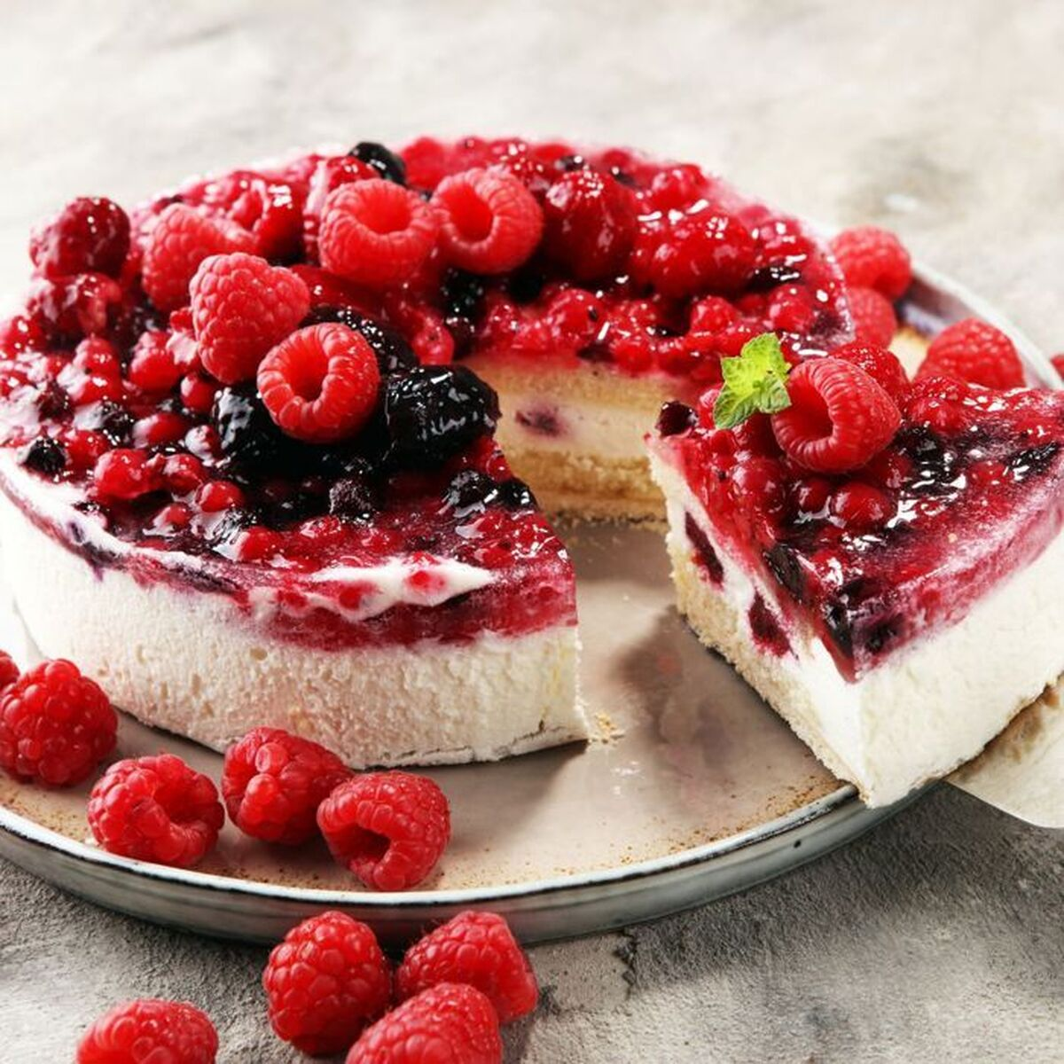 Käsekuchen mit roten Beeren belegt. Ein Stück ist entfernt. Himbeeren und Brombeeren sind sichtbar.