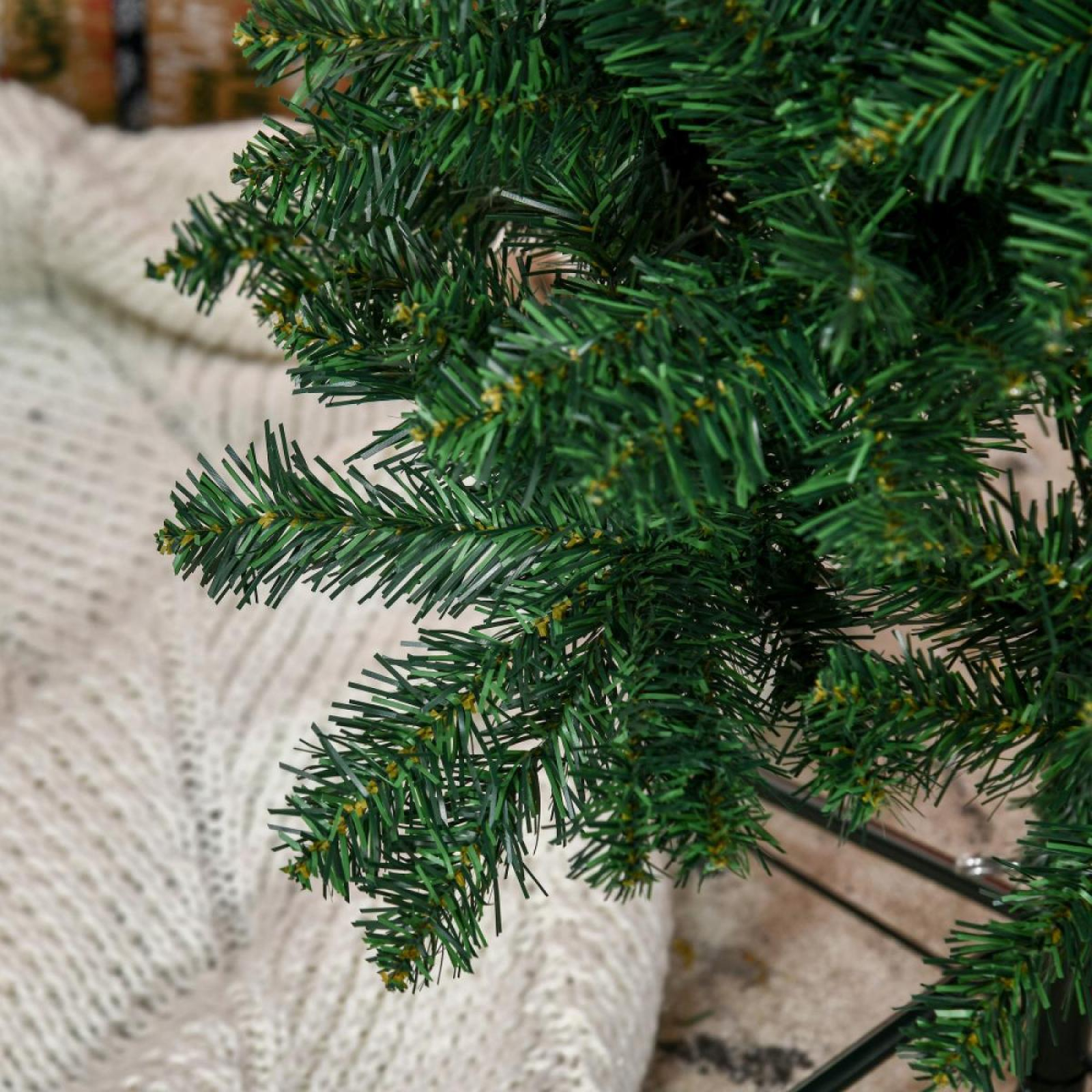 Nahaufnahme eines grünen künstlichen Weihnachtsbaumzweigs. Im Hintergrund befindet sich eine weiße Strickdecke.