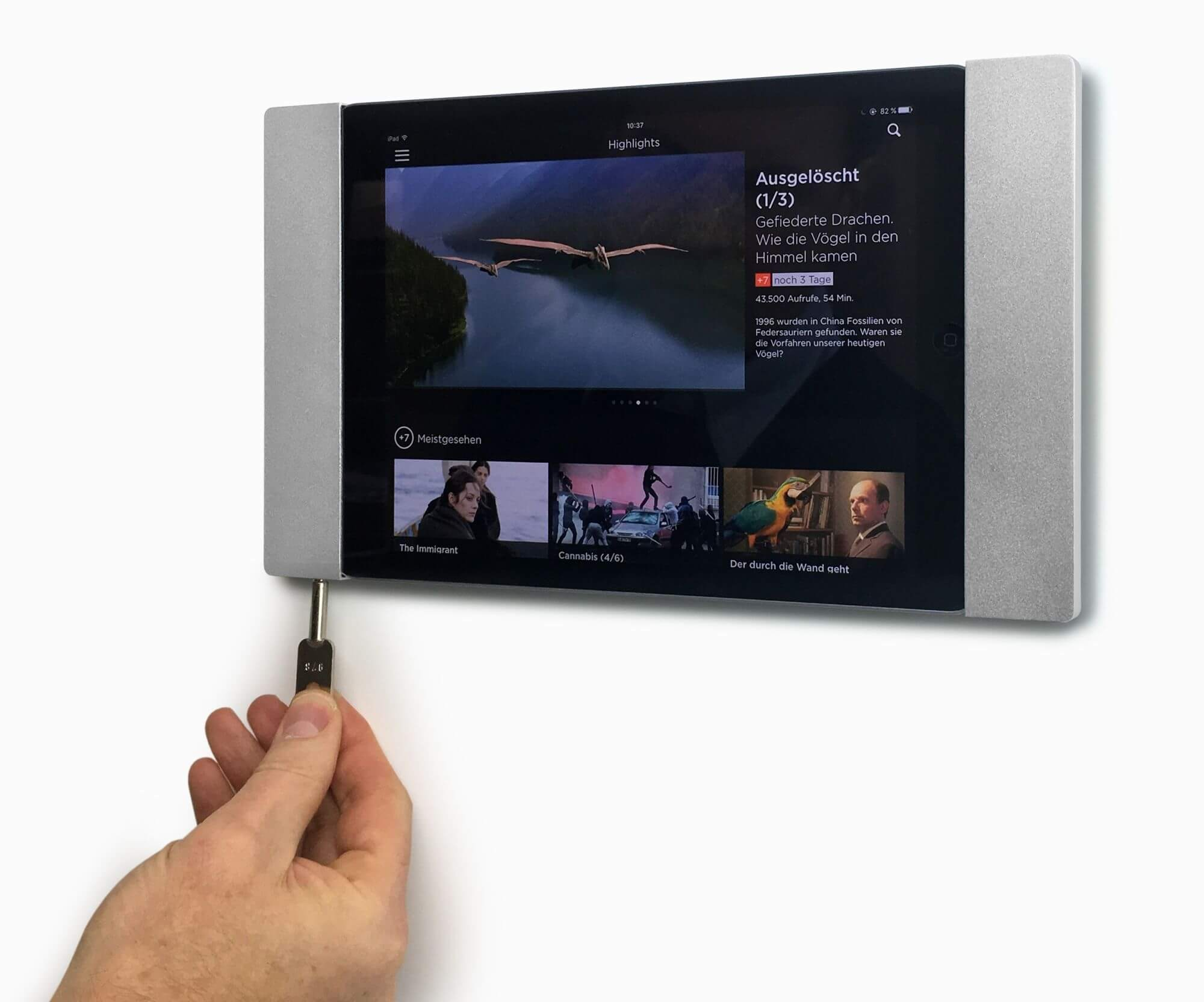 Ein Tablet ist an einer Wand montiert und zeigt ein Video. Eine Hand steckt ein Kabel in das Tablet.