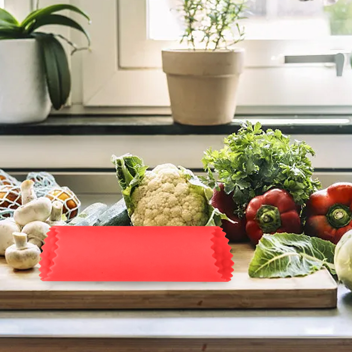 Ein Schneidebrett mit Gemüse wie Blumenkohl, roten Paprika und grünen Kräutern. Ein rotes Objekt im Vordergrund.