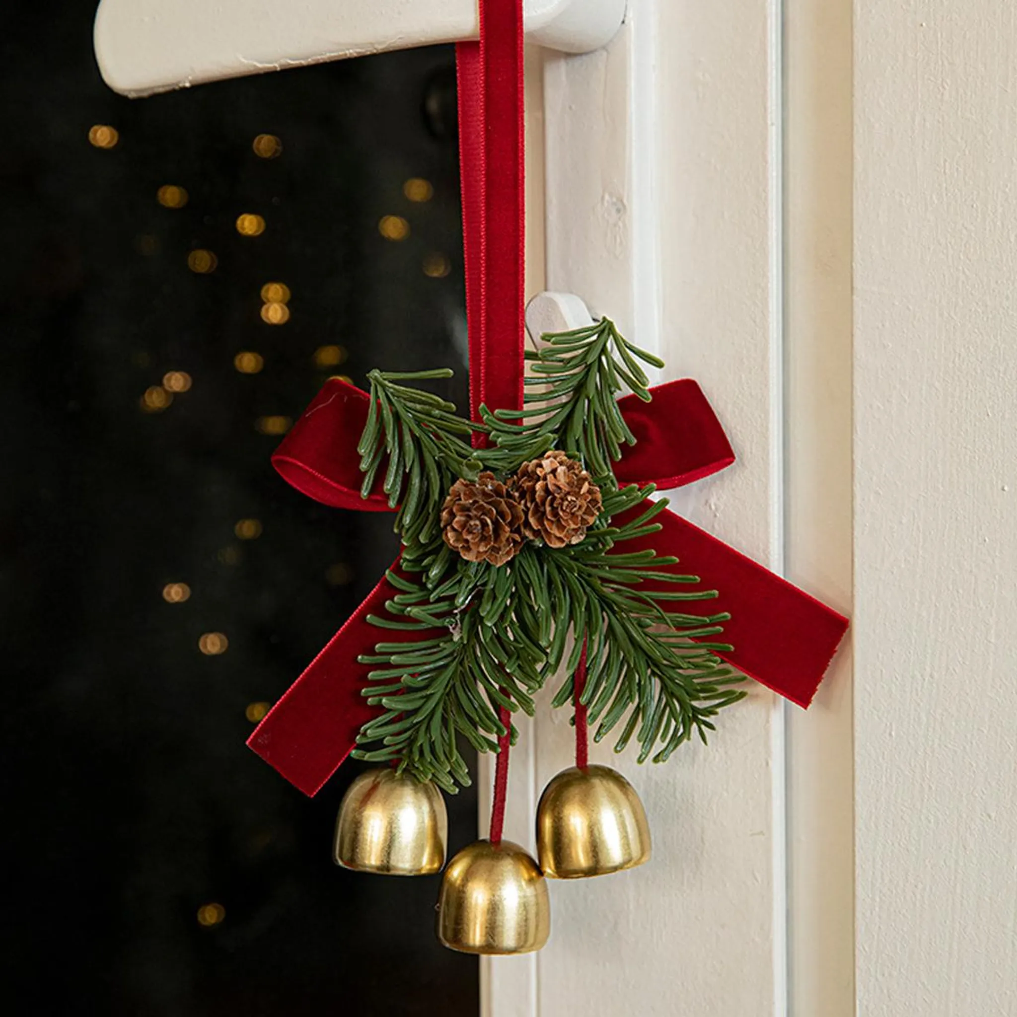 Eine Weihnachtsdekoration für die Tür mit Glocken, Tannenzapfen und rotem Band. Der Hintergrund ist ein verschwommenes Schwarz mit goldenen Lichtern.