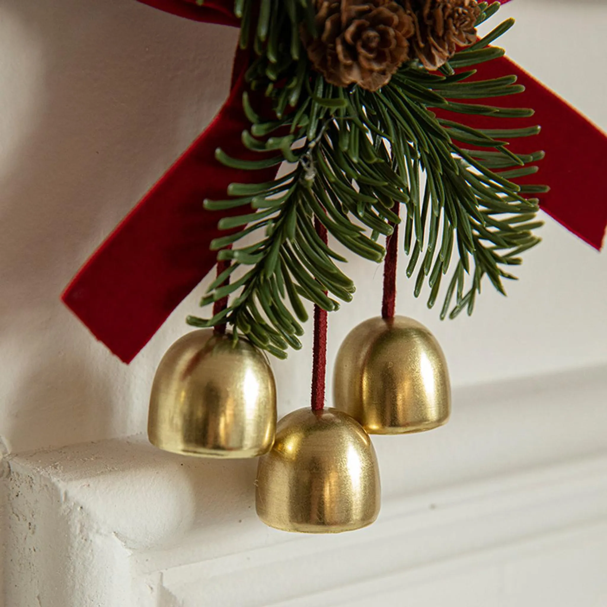 Nahaufnahme einer Weihnachtsdekoration. Drei goldene Glocken hängen an einem grünen Zweig und rotem Band. Weißer Hintergrund.