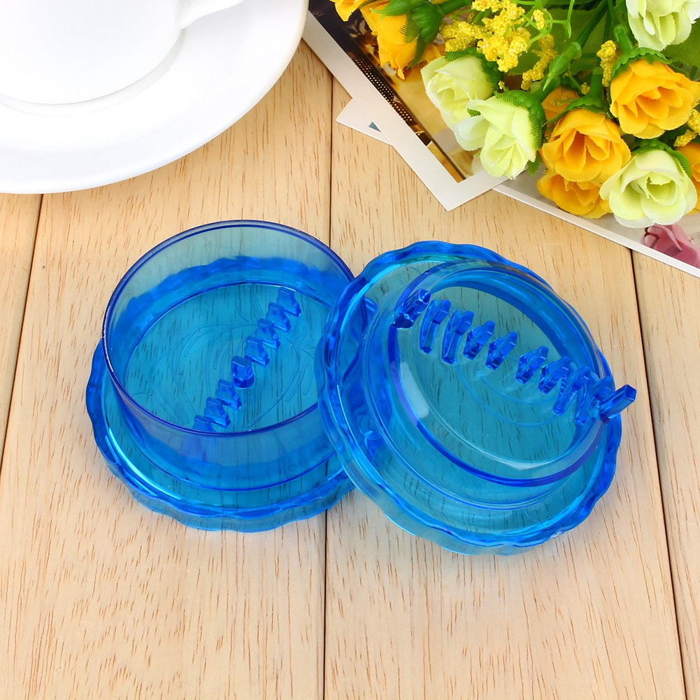 Zwei blaue Kunststoff-Grinder auf Holzoberfläche. Einer ist offen. Blumen und ein weißer Teller sind im Hintergrund.