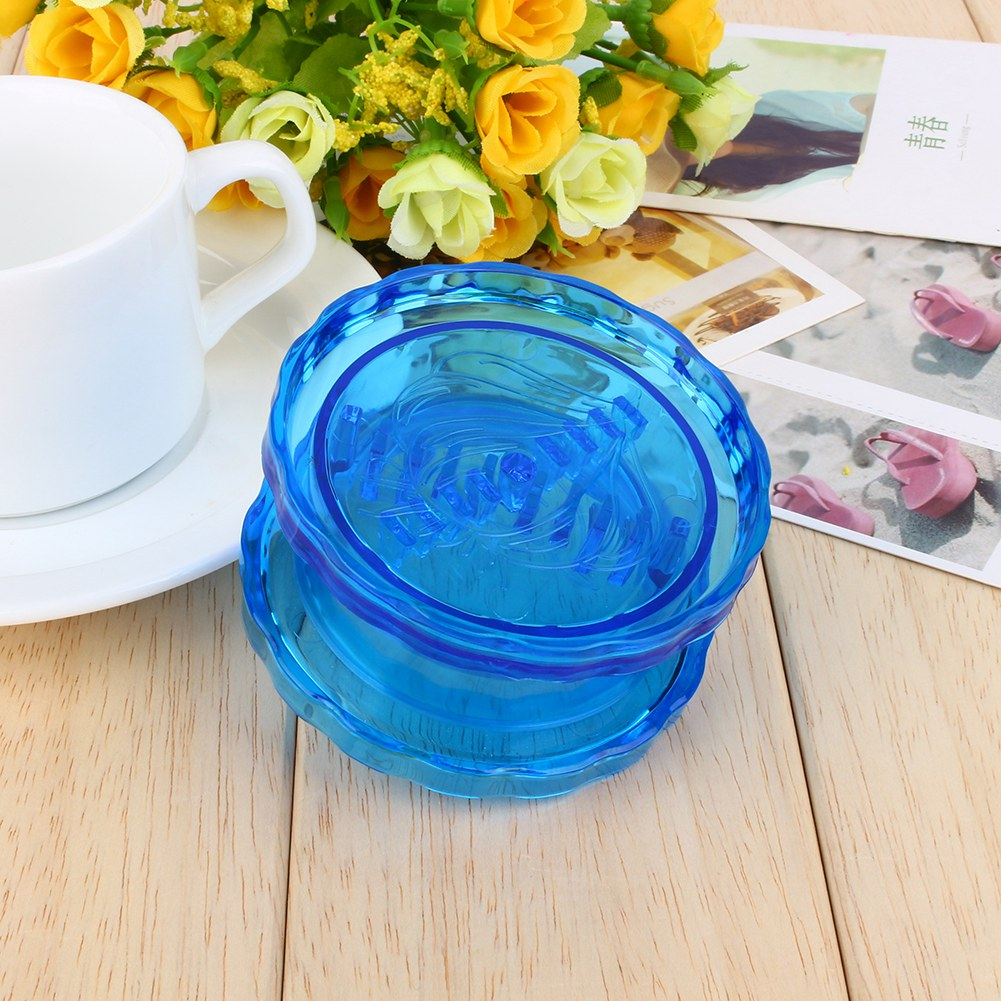 Ein blauer Grinder liegt auf Holz. Eine weiße Tasse, Untertasse und gelbe Blumen befinden sich im Hintergrund. Fotos sind ebenfalls vorhanden.