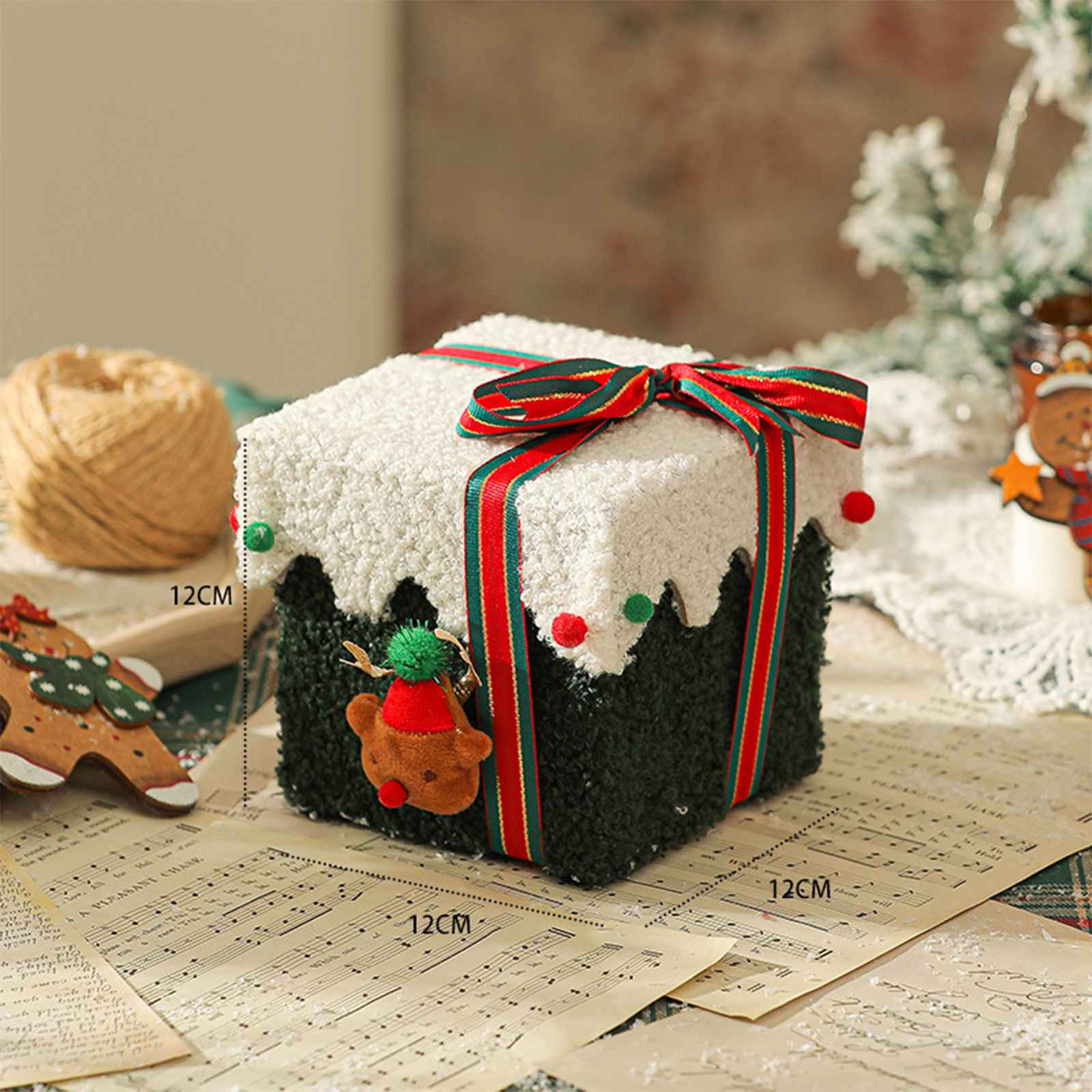 Eine quadratische Weihnachtsgeschenkbox mit weißer Oberseite und grünem Boden, rot-grünem Band, auf Notenblättern.