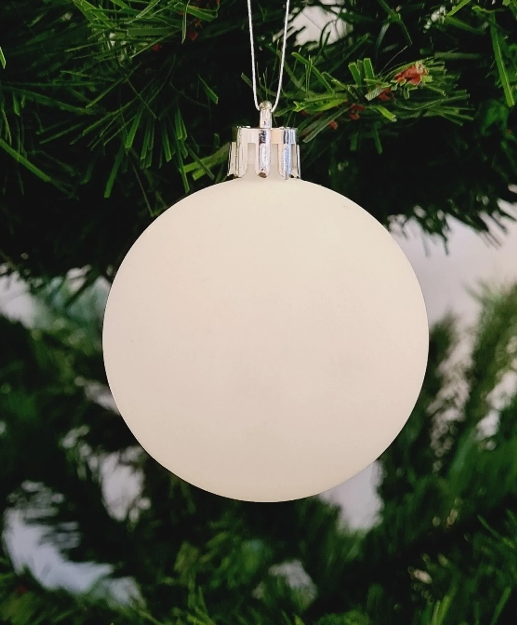 Ein weißer Weihnachtsschmuck hängt an einem grünen Weihnachtsbaum. Der Schmuck ist rund und glatt.