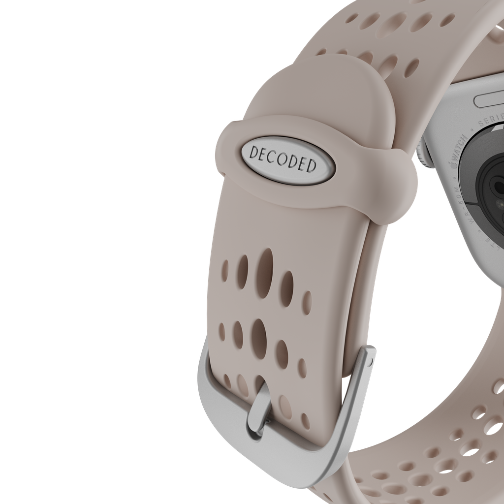 Primo piano di un cinturino con 'DECODED'. Il cinturino è beige con fori. È visibile una fibbia argentata. Si vede il retro dell'orologio.