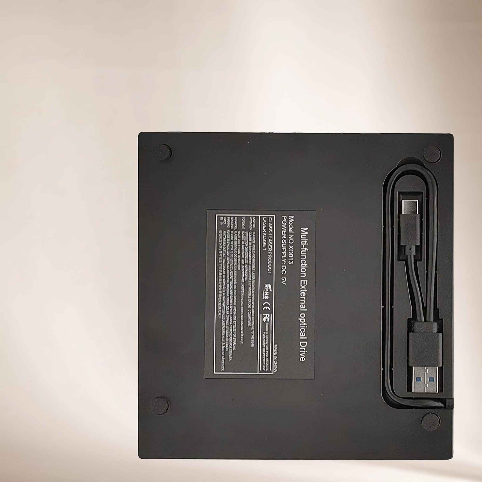 Schwarzes externes optisches Laufwerk mit USB-Kabel auf hellbeiger Oberfläche. Text auf dem Laufwerk zeigt Modell und Spezifikationen.
