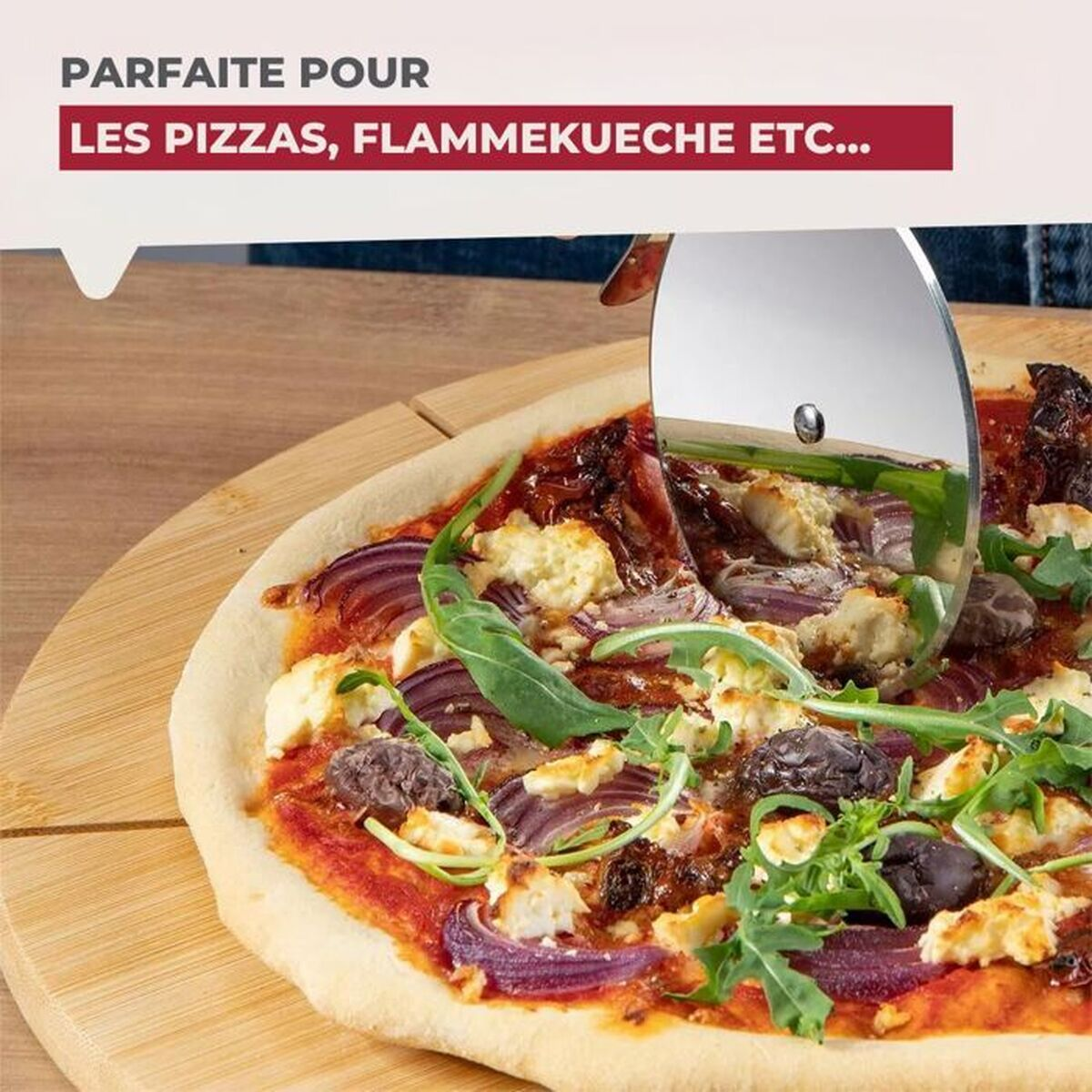 Eine Pizza mit Belag, die mit einem Pizzaschneider geschnitten wird. Rote Zwiebeln, Käse, Oliven und Grünzeug sind sichtbar.