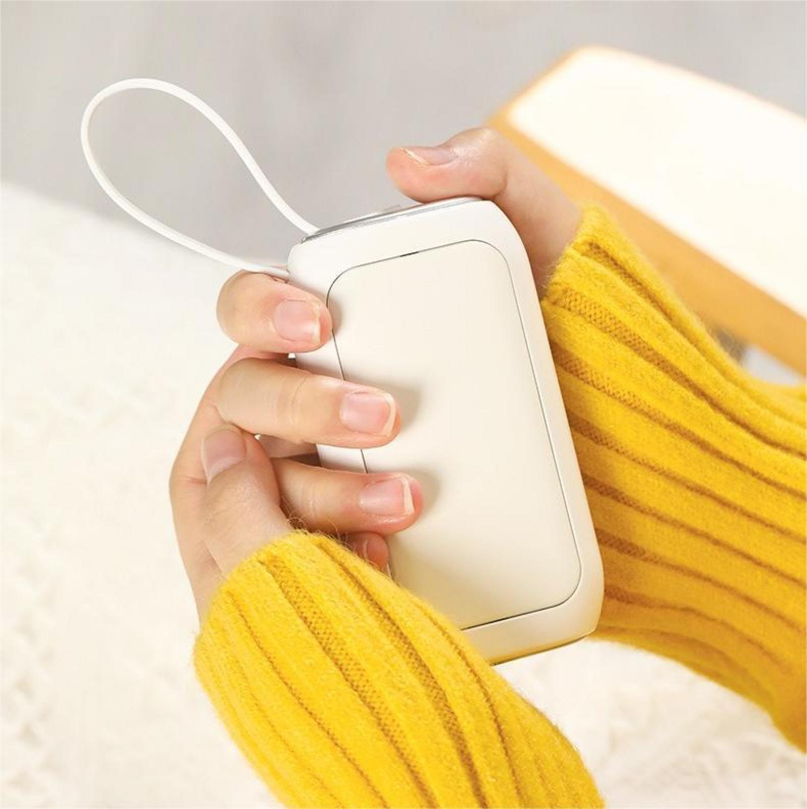 Eine Person hält ein weißes rechteckiges Gerät, möglicherweise eine Powerbank. Sie trägt einen gelben Pullover. Weiße Schleife am Gerät.