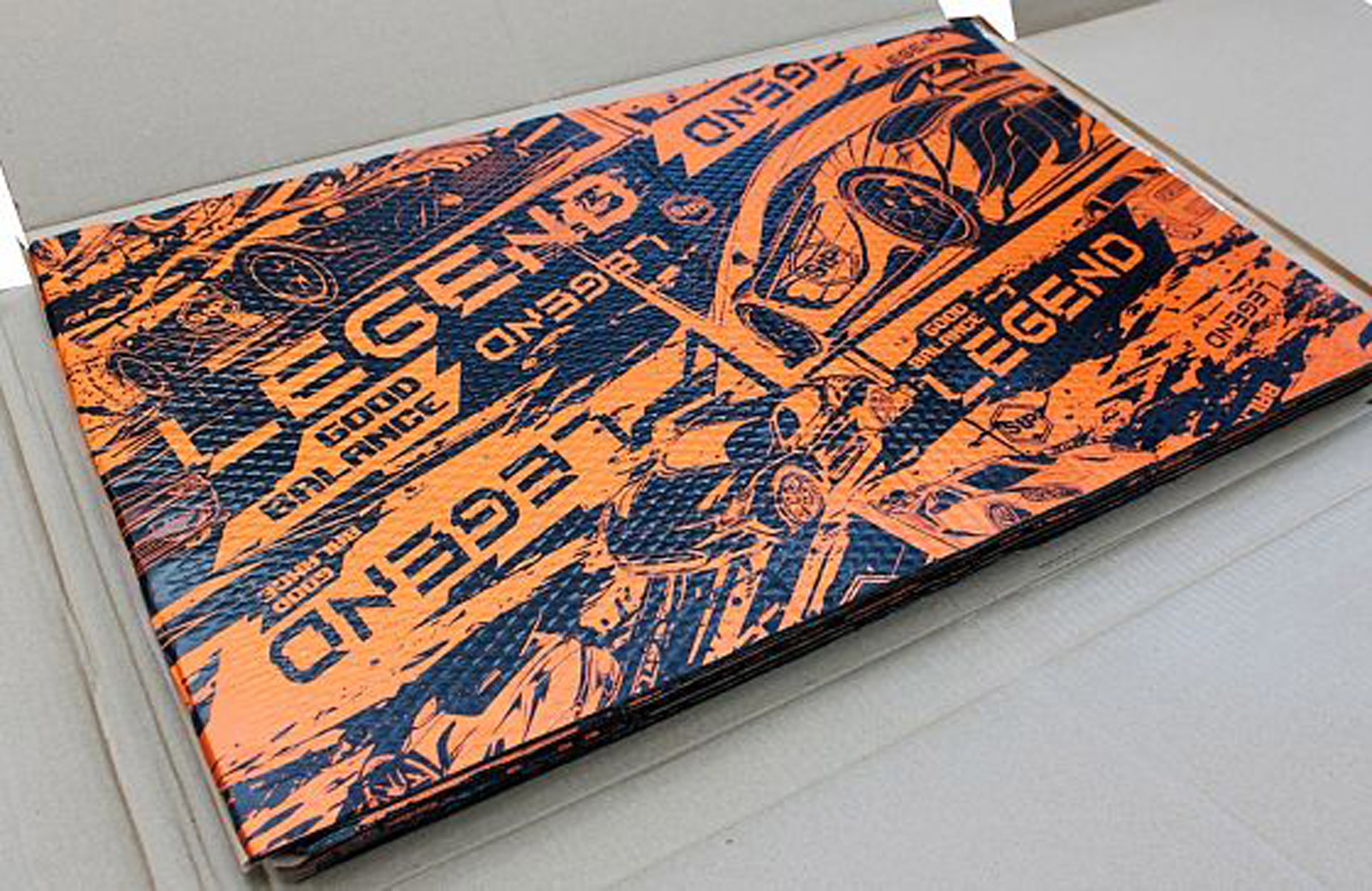 Ein orange-schwarzes Design eines Autos und das Wort LEGEND befindet sich auf einem rechteckigen Gegenstand in einem Karton.