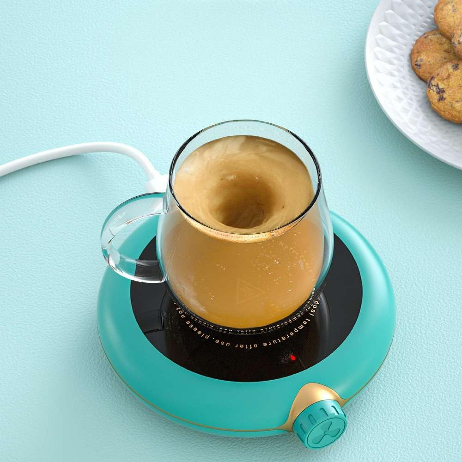 Eine Kaffeetasse auf einem türkisfarbenen Wärmer. Kaffee wirbelt in der durchsichtigen Tasse. Kekse auf einem weißen Teller im Hintergrund.