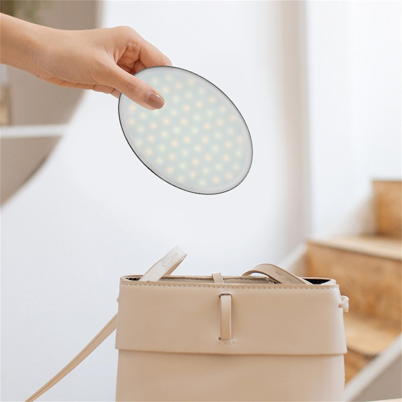 Hand hält eine beleuchtete ovale Platte über einer beigen Handtasche. Das Panel hat viele kleine Lichter.