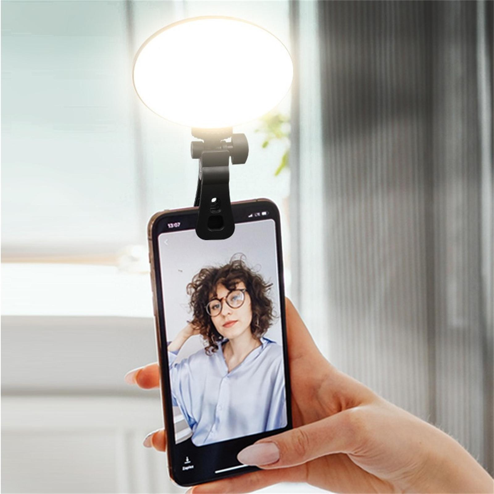 Ein Telefon mit angebrachtem Licht in der Hand, das eine Frau mit Brille zeigt. Licht scheint auf das Telefon.