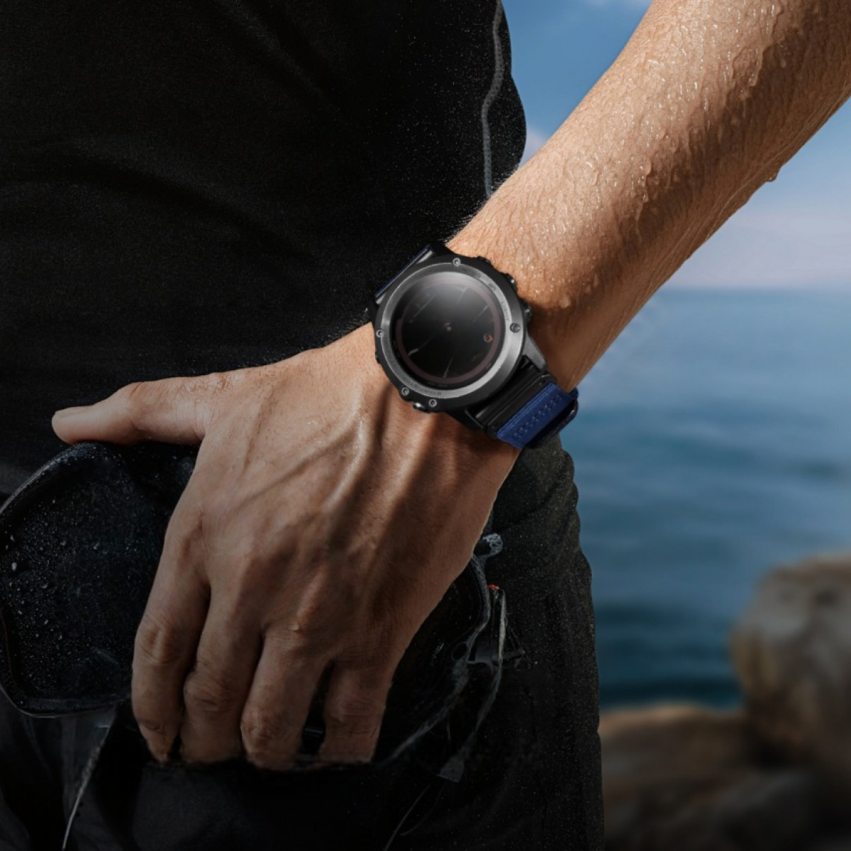 Eine Person, die eine schwarze Smartwatch mit blauem Armband trägt. Die Person hält etwas Dunkles in der anderen Hand, in der Nähe von Wasser.
