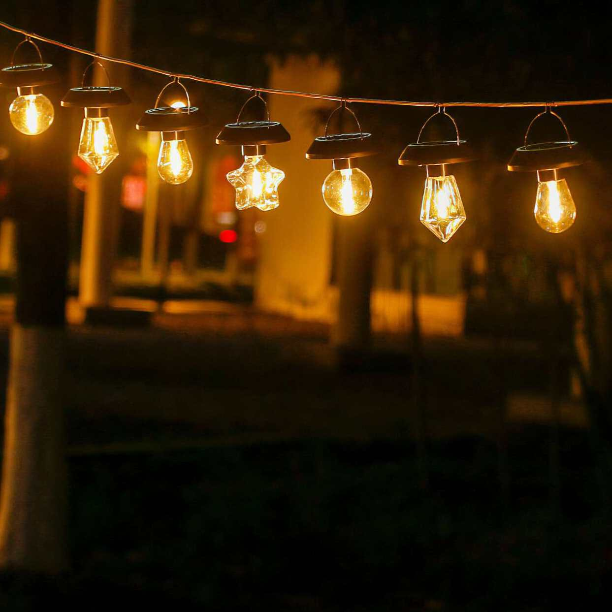Lichterketten mit verschiedenen Glühbirnenformen hängen vor dunklem Hintergrund und sind mit warmem Licht beleuchtet.