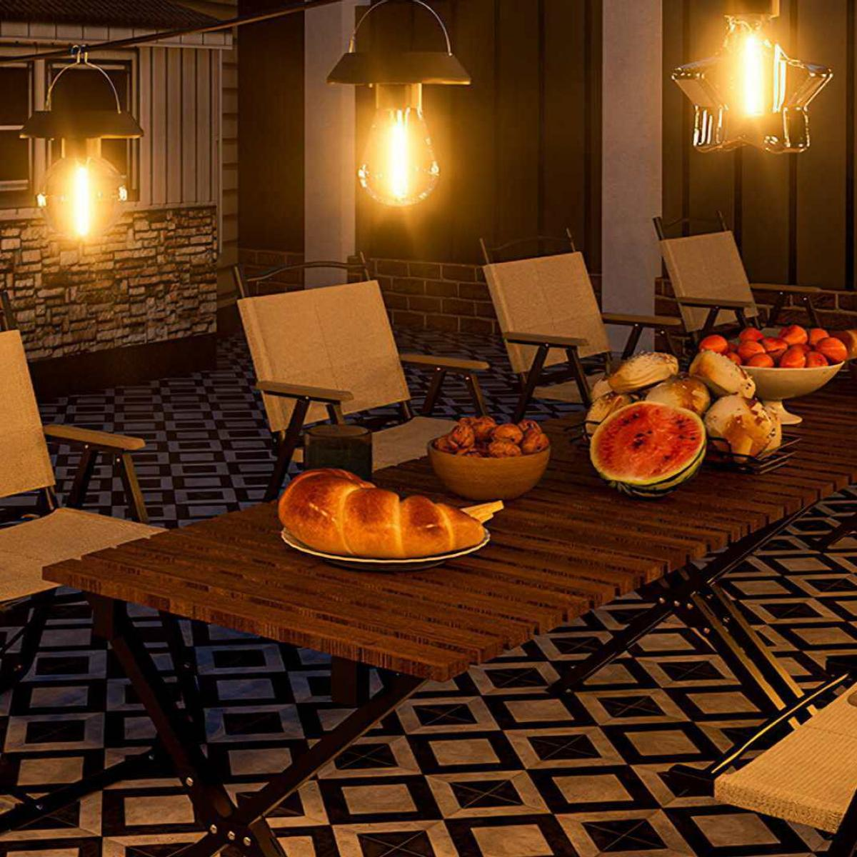 Ein Tisch ist mit Brot, Obst und Wassermelone unter Hängelampen gedeckt. Stühle umgeben den Tisch auf einer gefliesten Terrasse.