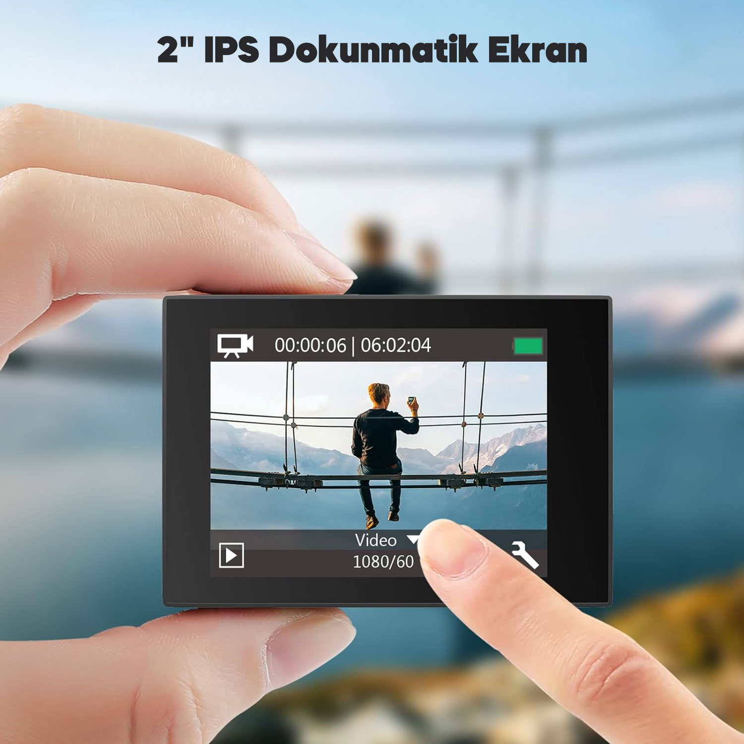 Bir el, bir köprüde oturan bir adamın video kaydını, arka planda dağları gösteren siyah bir aksiyon kamerası tutuyor.