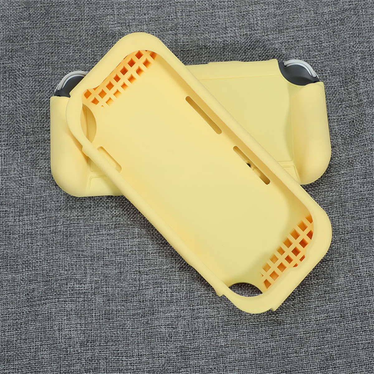Zwei gelbe Nintendo Switch Lite Hüllen auf einer grauen Stoffoberfläche. Eine Hülle bedeckt teilweise die andere.
