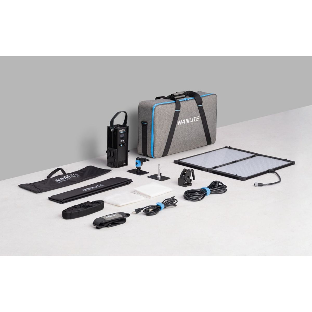 Una borsa grigia NANLITE e accessori sono disposti. Include una luce, cavi e vari elementi di supporto su una superficie bianca.
