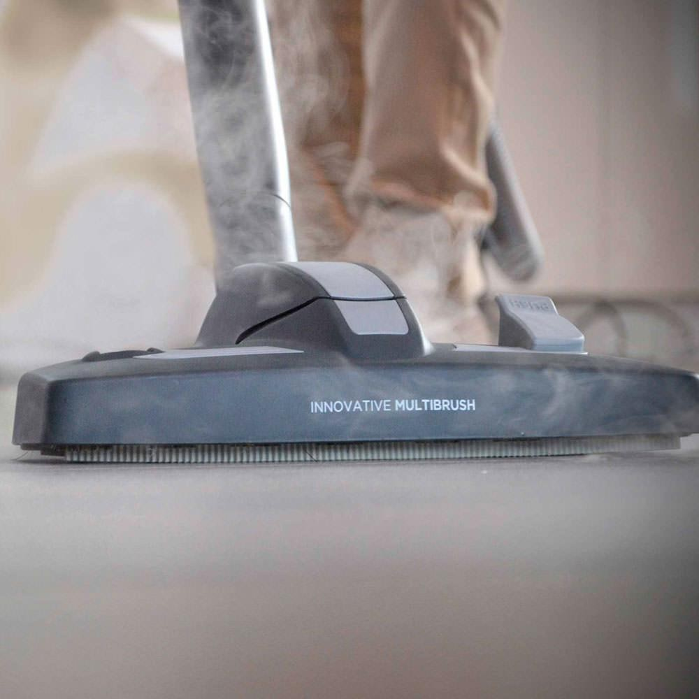 Nahaufnahme eines Staubsaugerkopfes mit dem Aufdruck 'INNOVATIVE MULTIBRUSH'. Dampf steigt von der Bürste auf.