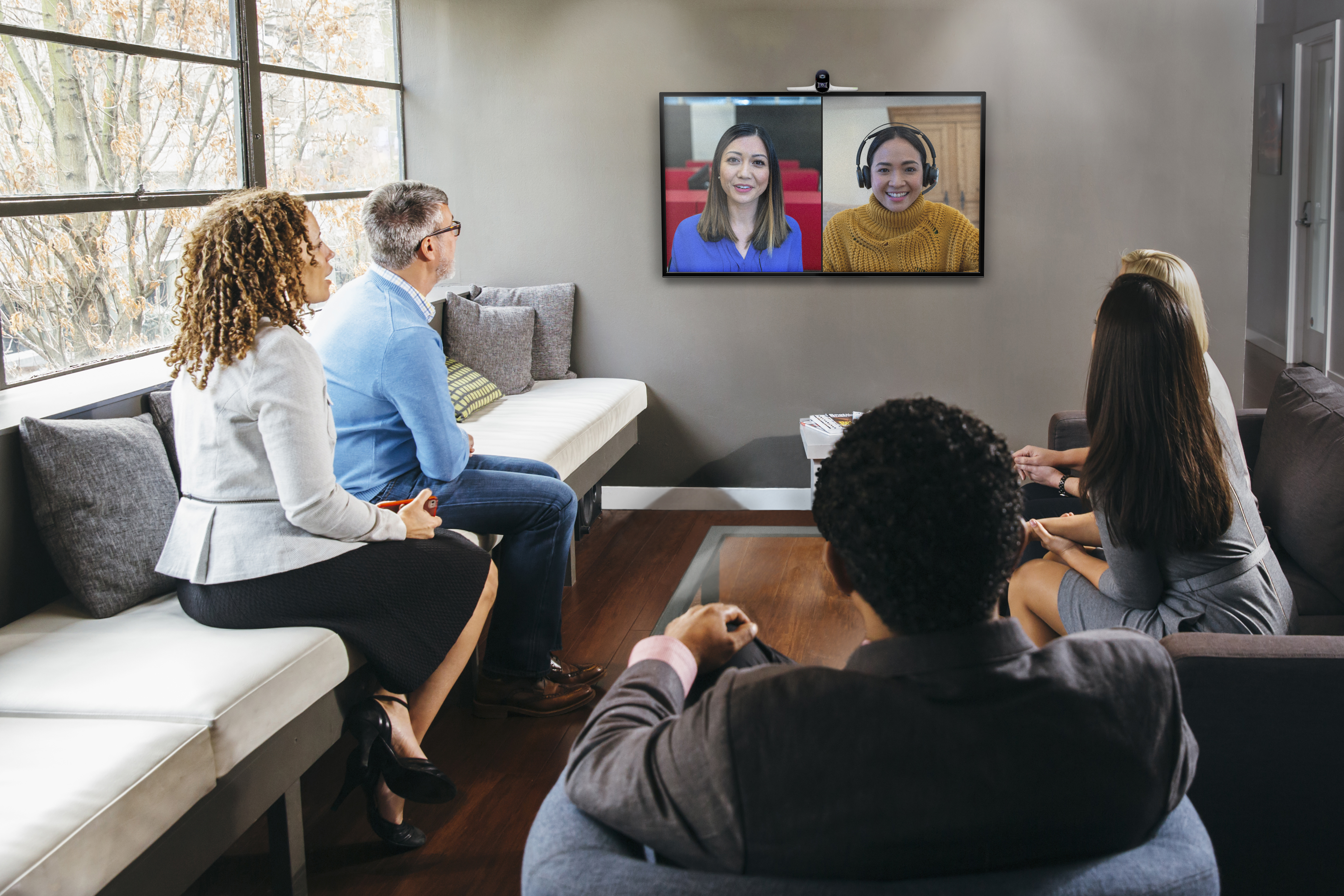Persone in una sala riunioni, guardando una videochiamata. Due donne sono sullo schermo.