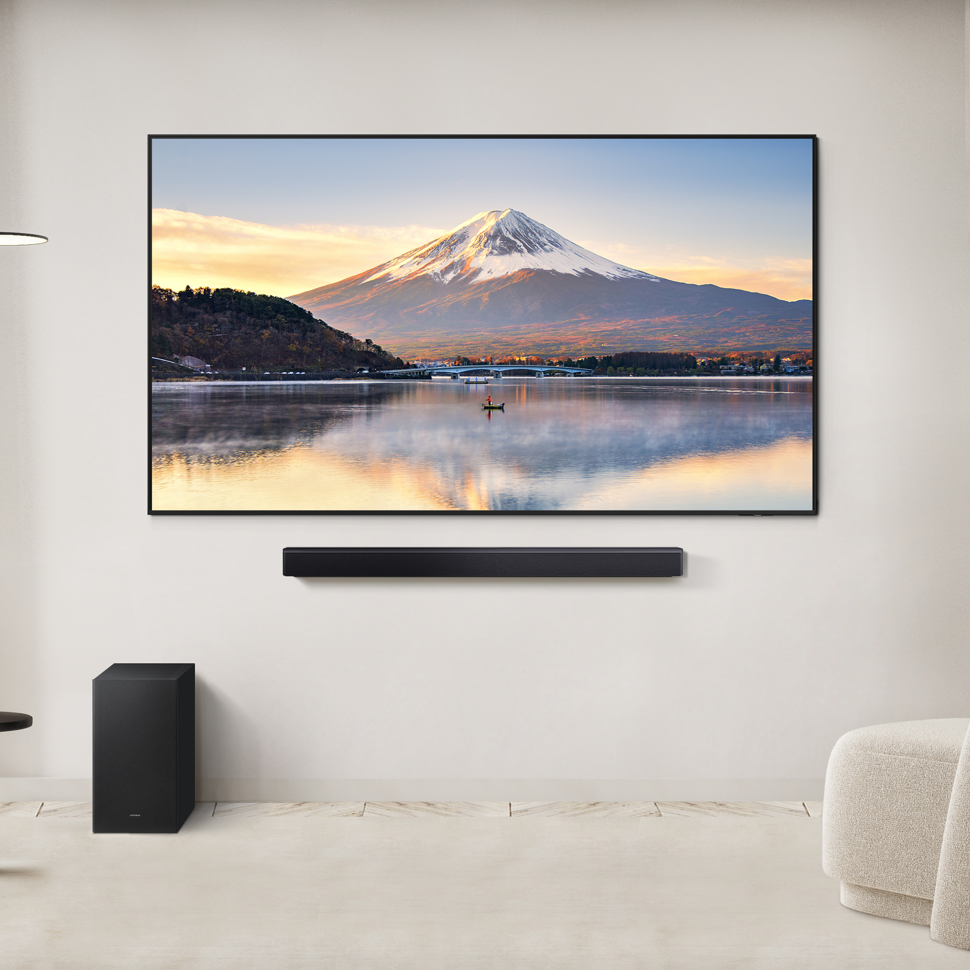 Een tv toont een landschap. Daaronder een soundbar. Een subwoofer links. Een beige stoel rechts.