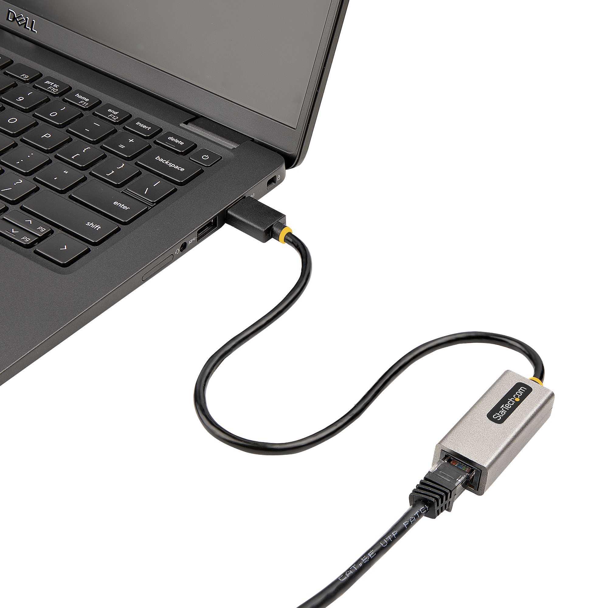 Un portátil con cable negro conectado. El cable va a un adaptador StarTech plateado. Fondo blanco.