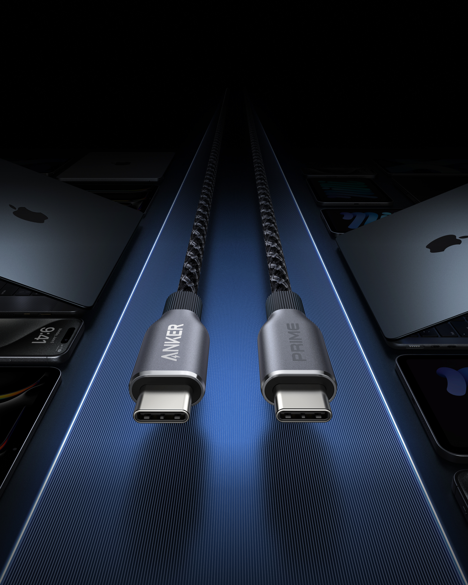 Due cavi USB-C Anker Prime, intrecciati, connettori argentati, su una superficie blu. Laptop e telefoni sullo sfondo.