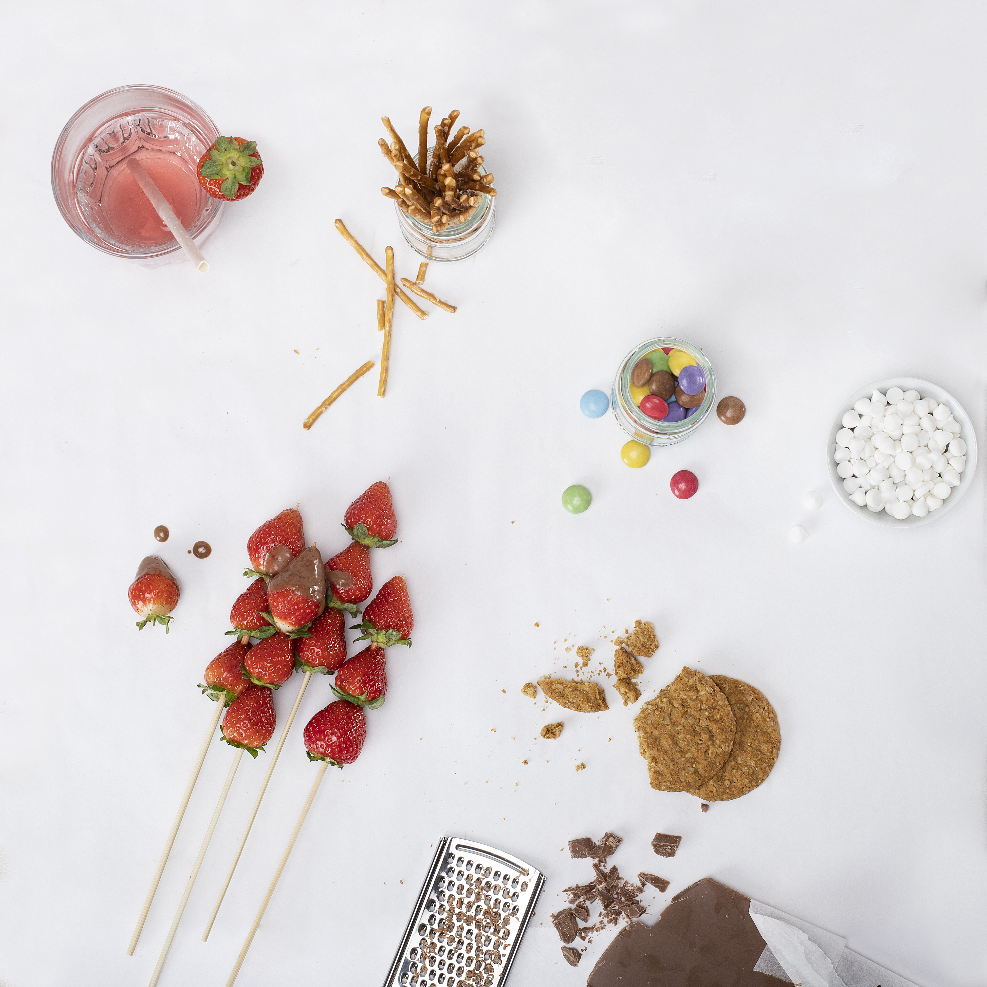 Draufsicht verschiedener Snacks: Erdbeeren, Schokolade, Brezeln, Kekse, Süßigkeiten und ein rosa Getränk.