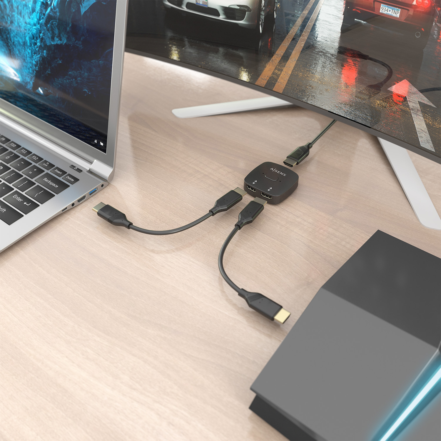 Un laptop, un monitor e uno switch HDMI nero sono su una scrivania di legno. I cavi collegano i dispositivi. Un'auto è visibile sul monitor.