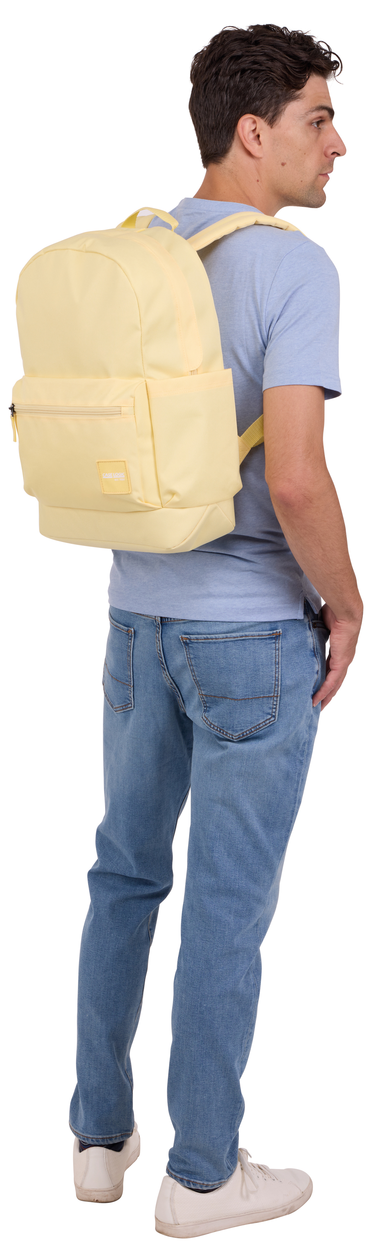 Homme en chemise et jean bleu clair, sac à dos jaune, chaussures blanches, de côté.