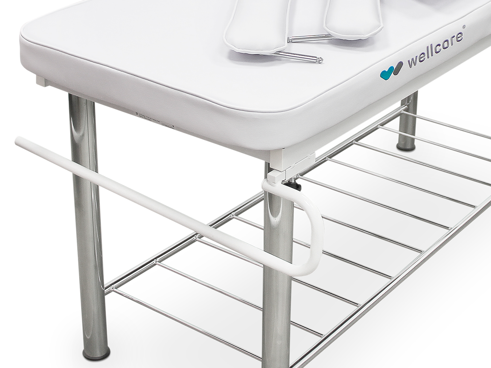 Una mesa médica blanca con una parte superior acolchada y patas cromadas. Tiene un estante inferior y un riel lateral. Dos reposacabezas blancos encima.