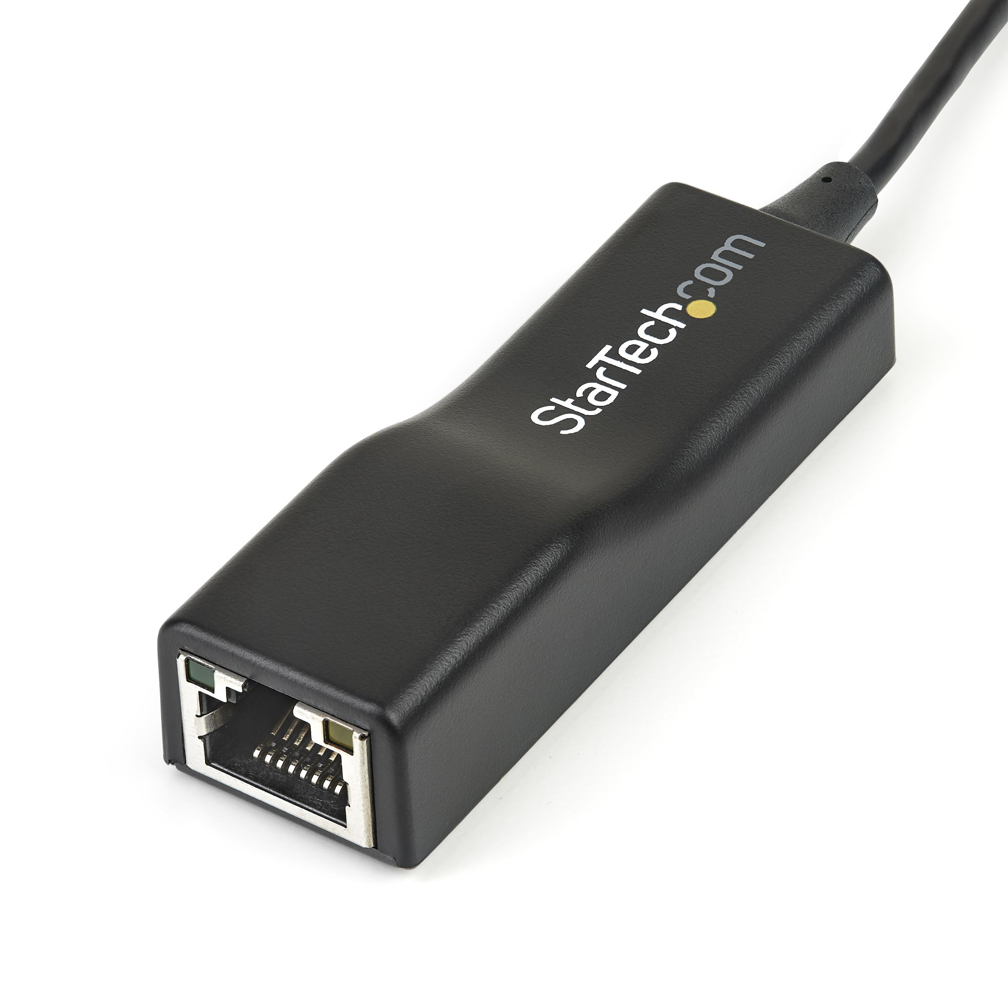 Adaptador Ethernet StarTech negro con cable, sobre superficie blanca, con el nombre de la marca en el dispositivo.