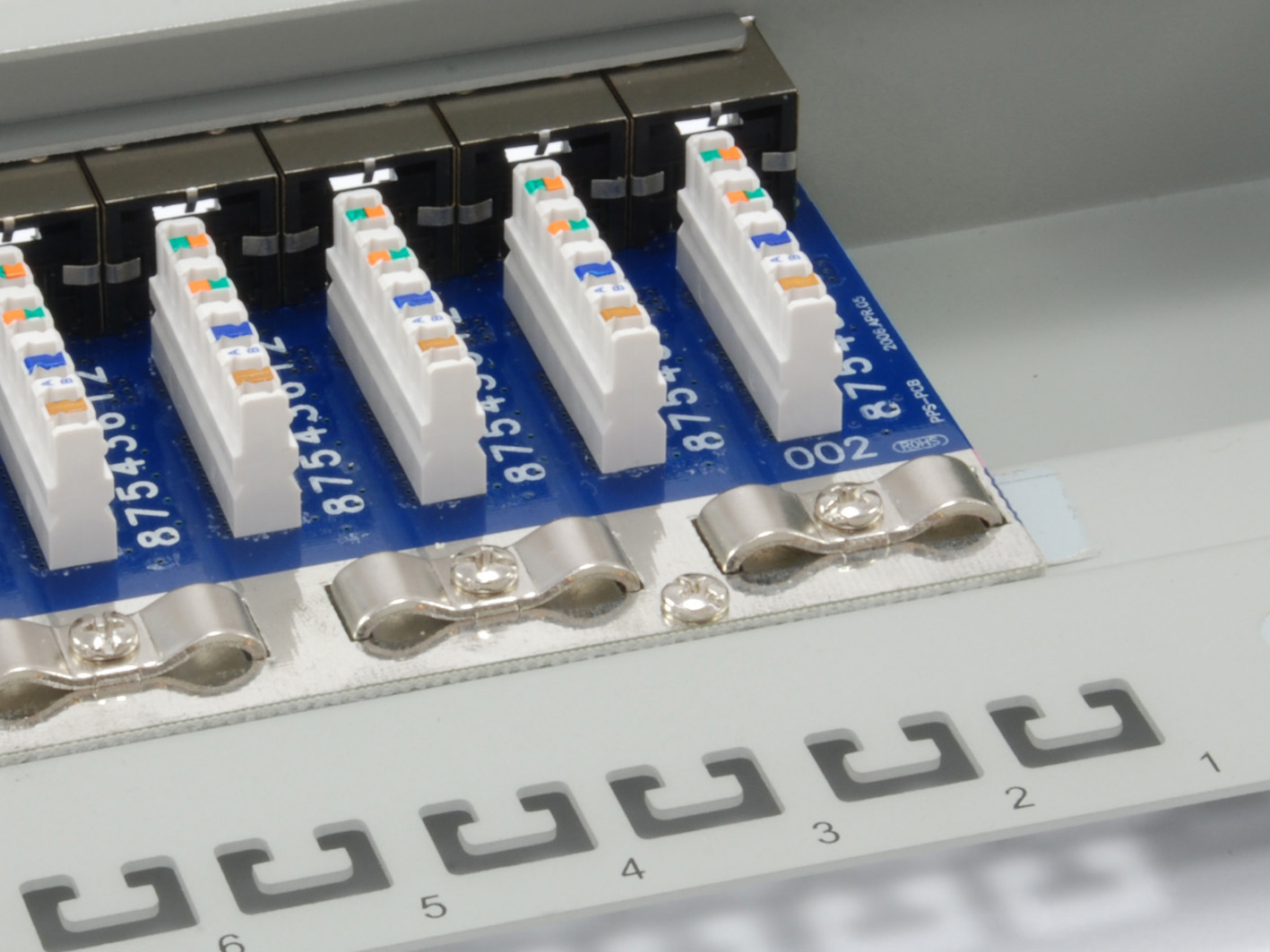 Zbliżenie panelu krosowego sieci z białymi złączami, niebieskimi płytkami obwodów drukowanych oraz srebrnymi metalowymi zaciskami i śrubami. Widoczne są numery.