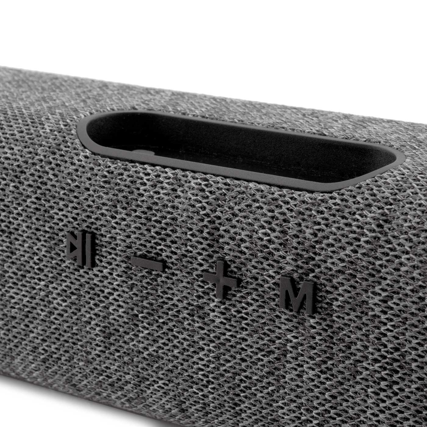 Primer plano de un altavoz gris con botones de control y un hueco negro en la parte superior. Los botones incluyen reproducción, volumen y modo.