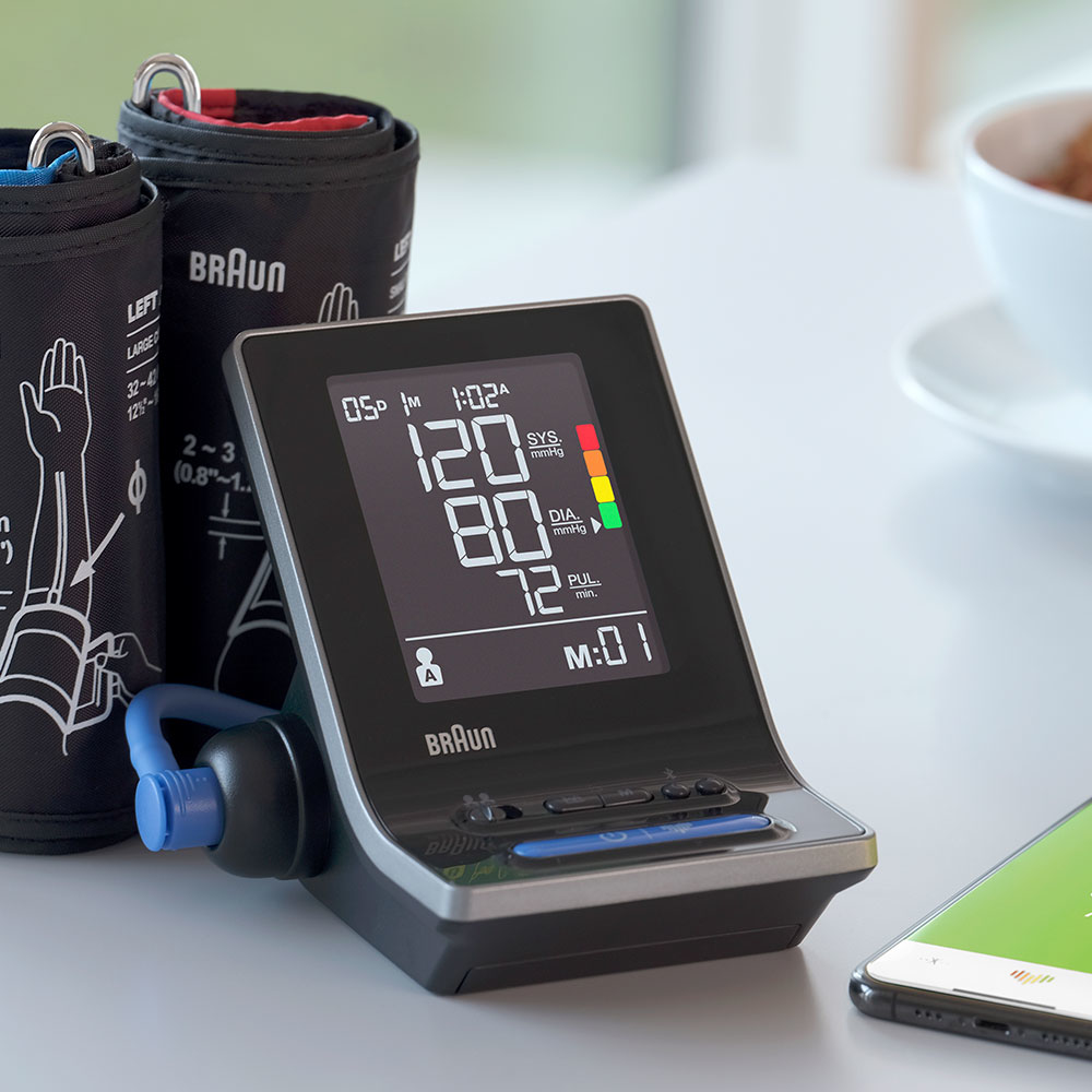 Ciśnieniomierz wyświetla odczyty 120/80, z mankietem i smartfonem w tle. W tle znajduje się filiżanka.