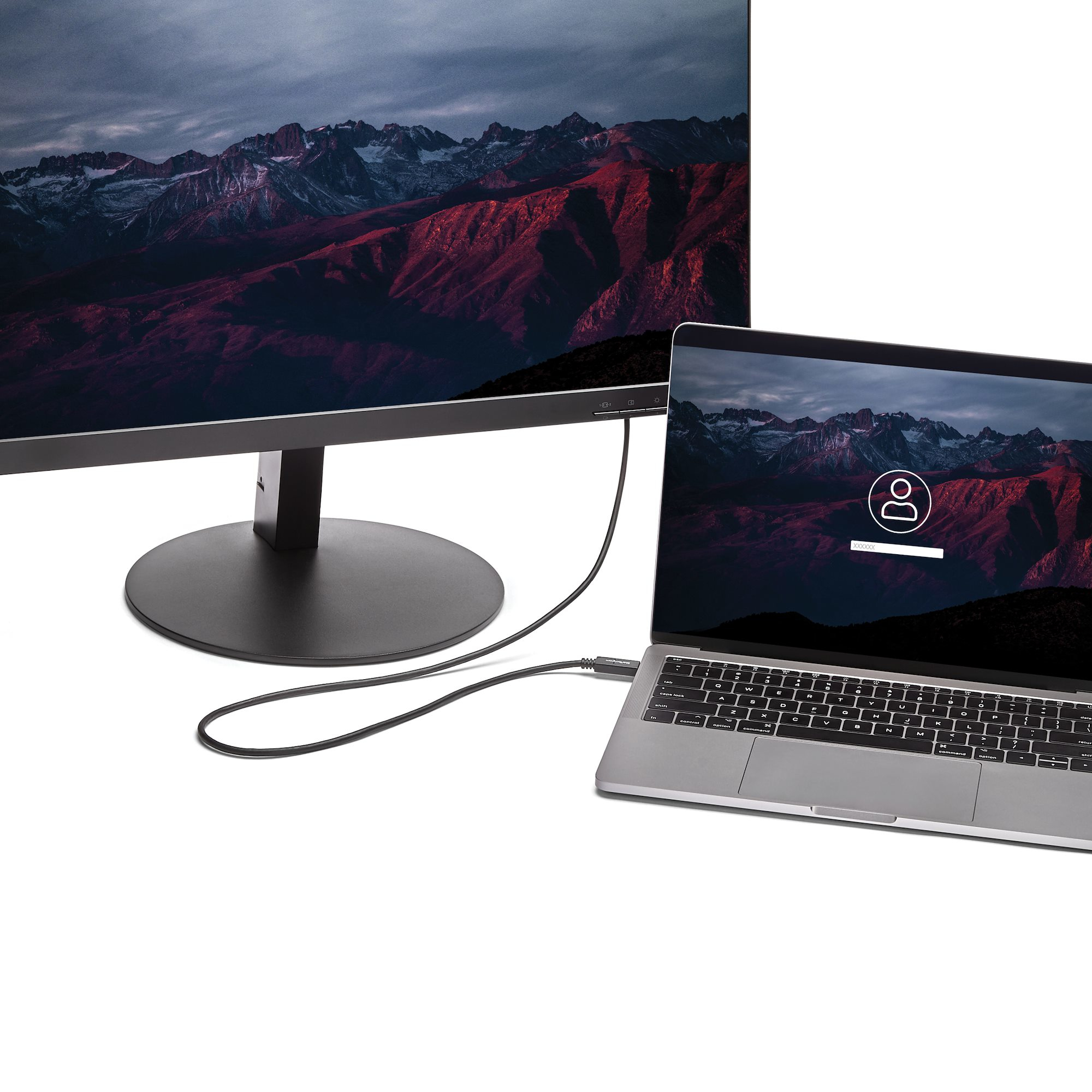 Portátil conectado a un monitor que muestra montañas. Pantalla de inicio de sesión en el portátil. Cable conecta los dispositivos.