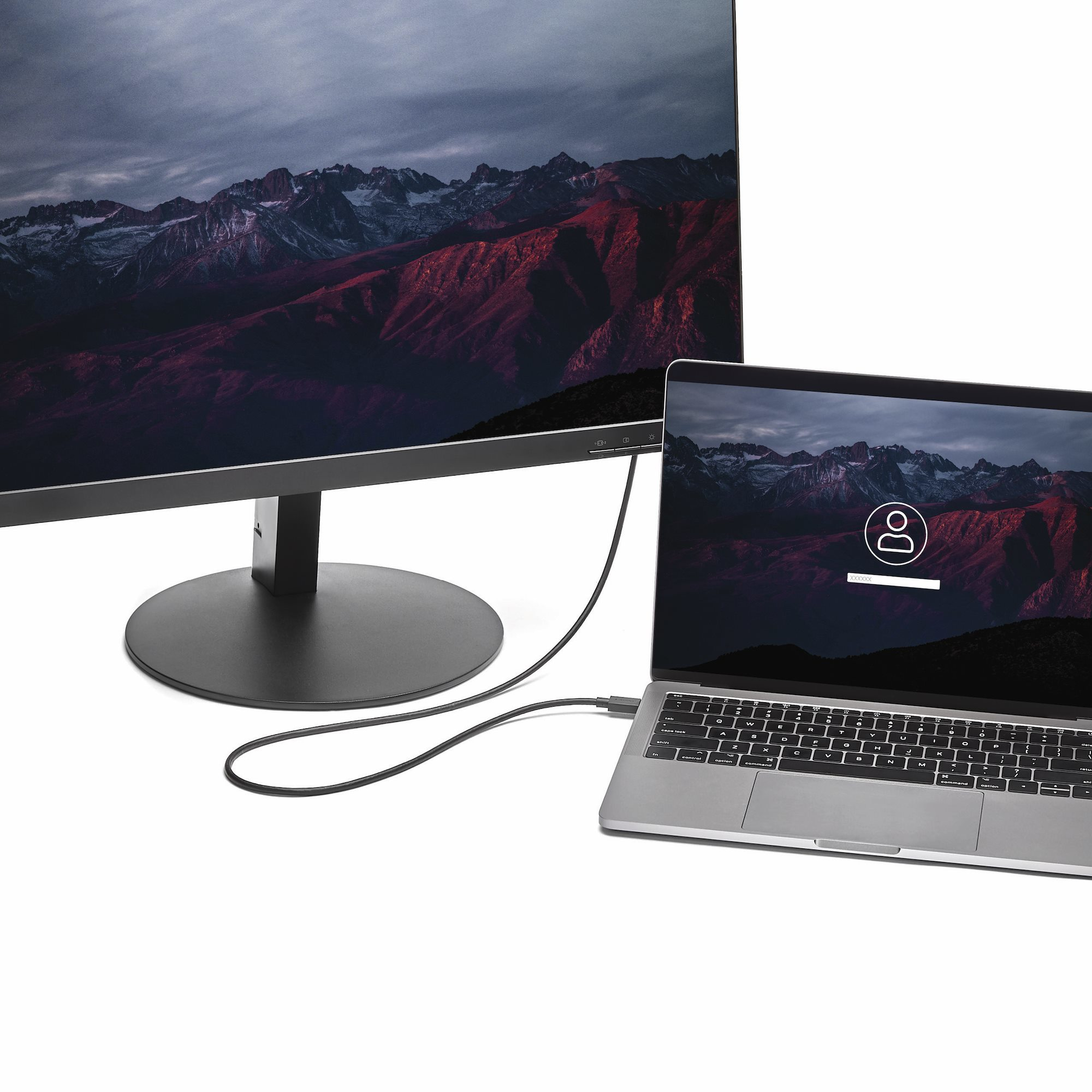 Una computadora portátil y un monitor conectados por un cable negro, ambos mostrando una escena de montaña. La laptop muestra una pantalla de inicio de sesión.