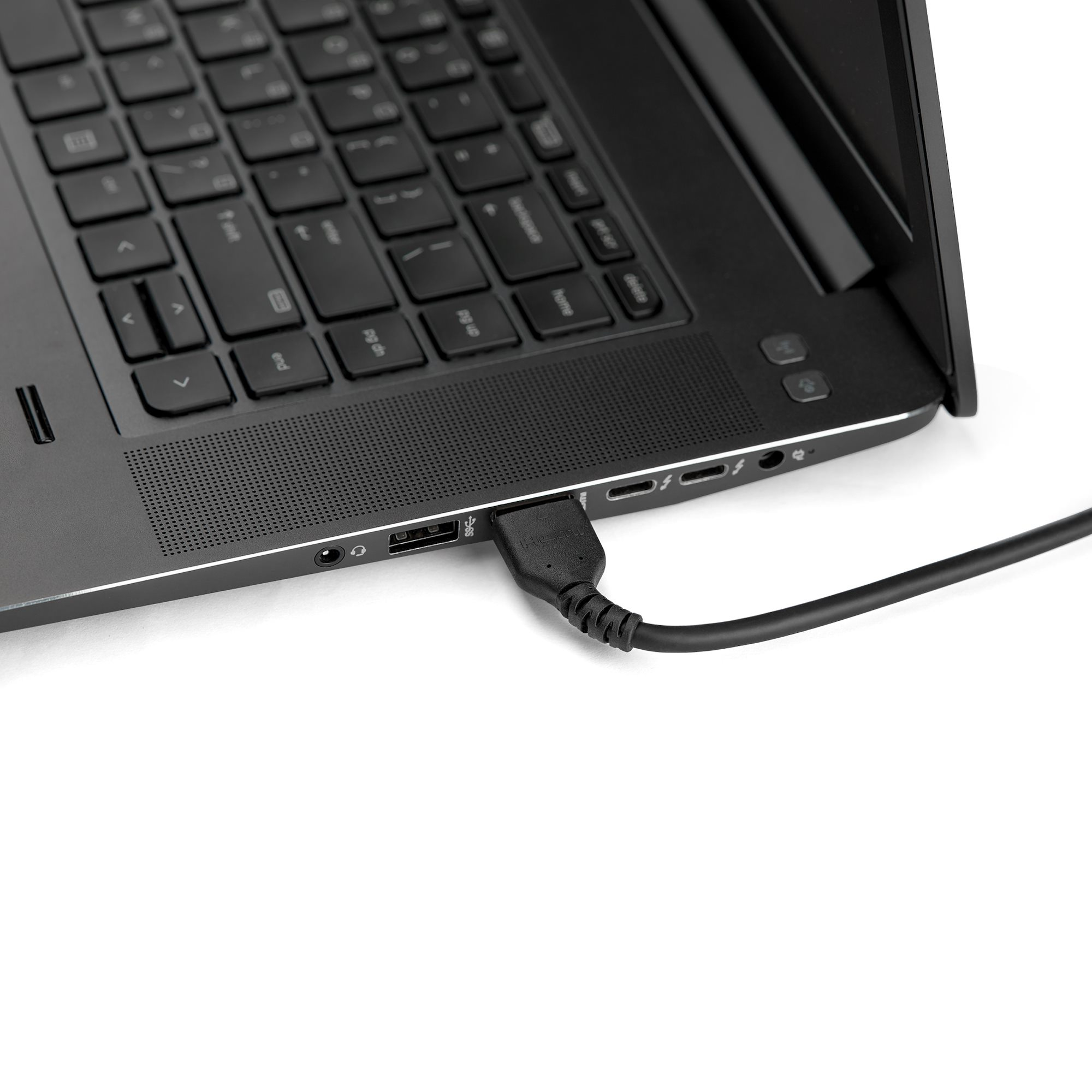 Portátil negro con cable USB enchufado. Teclado visible. Fondo blanco.