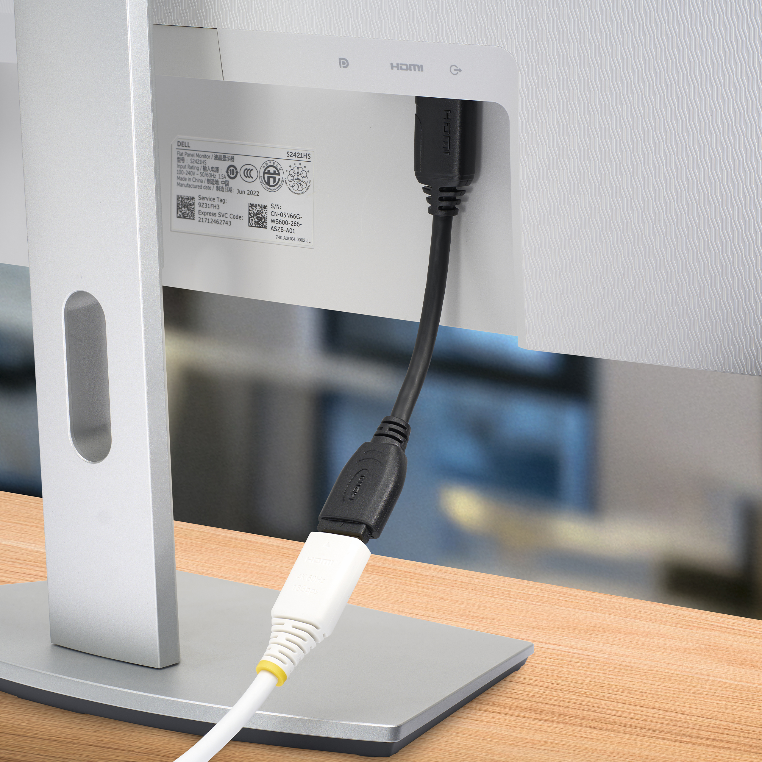 Un monitor con cable HDMI conectado. El cable es blanco y negro, y el monitor plateado.